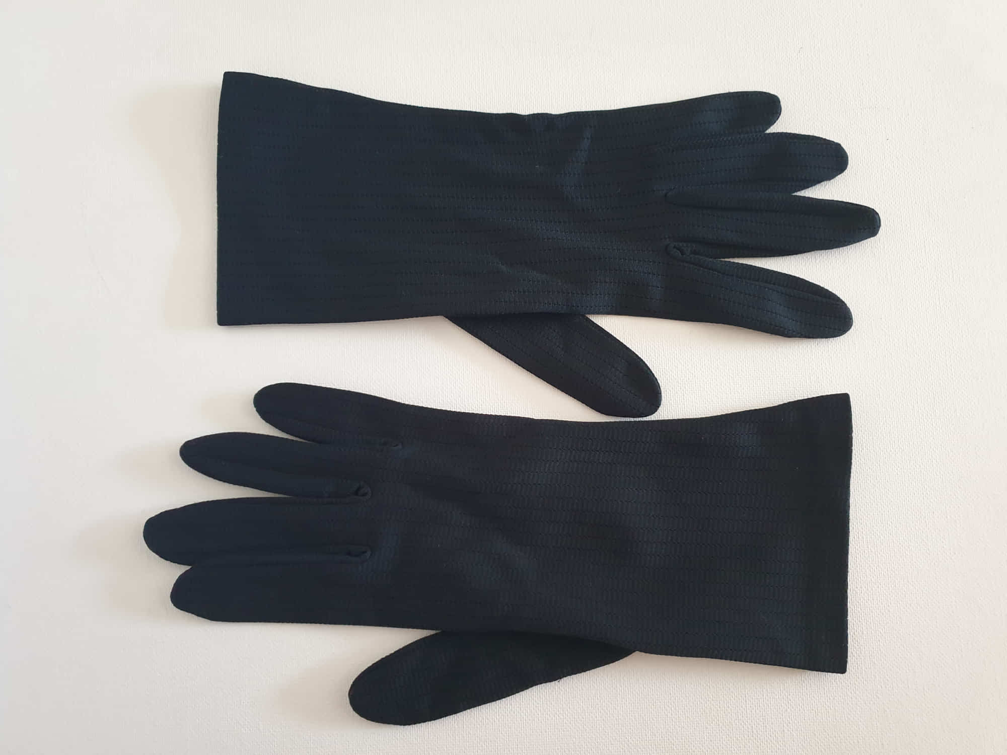 Smart black gloves for a classic dressed up look. Below wrist length stretch gloves have a striped pattern in the weave with a tiny transparent line, giving the look of a line of fine scoring. Mid weight. Fabric is nylon. No brand tag - 1960s. Large.