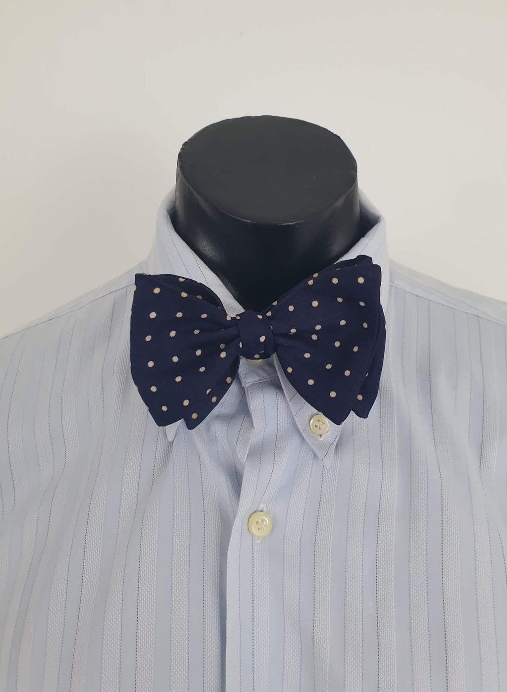 Navy blue polka dot self-tie bow tie has adjustable length. Ivory spots on navy blue ground.  Fabric is silk. Made in England - 1960s. Blade width 7.5 cm (3")