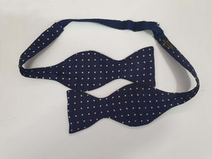 Navy blue polka dot self-tie bow tie has adjustable length. Ivory spots on navy blue ground.  Fabric is silk. Made in England - 1960s. Blade width 7.5 cm (3")