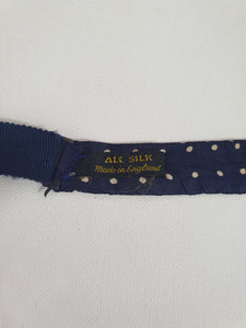 Navy blue polka dot self-tie bow tie has adjustable length. Ivory spots on navy blue ground.  Fabric is silk. Made in England - 1960s. Blade width 7.5 cm (3")