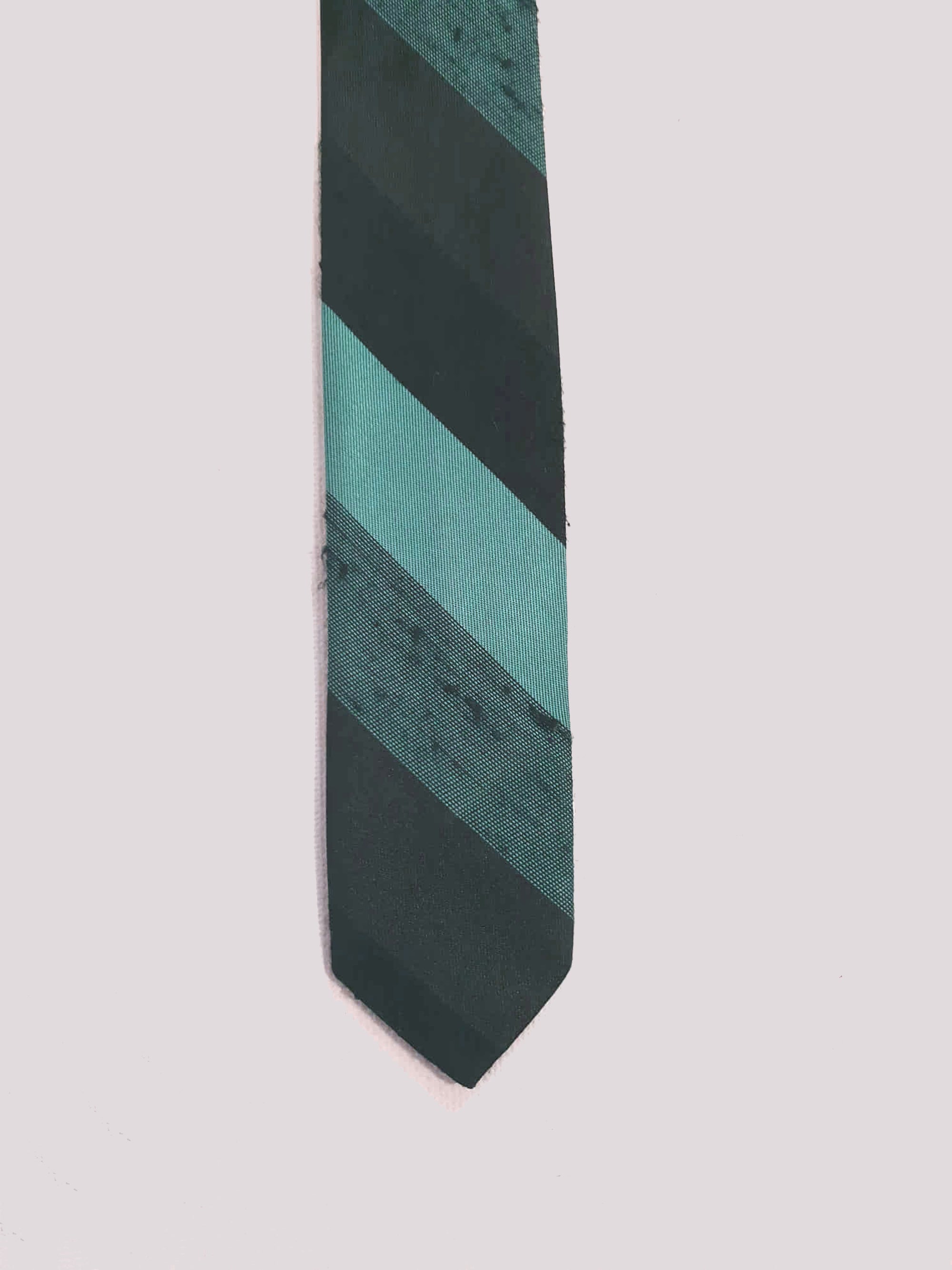 Super skinny tie in shades of grey-blue, grey and black. The grey band has a black fleck. Fabric is 100% polyester. Label reads "Superloom by Rodney" - 1960s. Blade width 3.7 cm (1.5") Length 130 cm (51") Excellent condition.