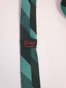 Super skinny tie in shades of grey-blue, grey and black. The grey band has a black fleck. Fabric is 100% polyester. Label reads "Superloom by Rodney" - 1960s. Blade width 3.7 cm (1.5") Length 130 cm (51") Excellent condition.