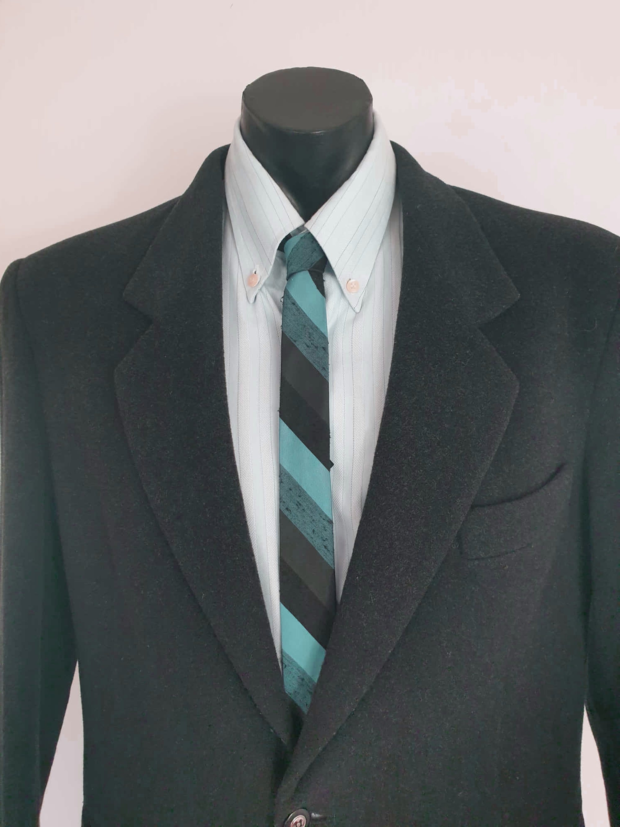 Super skinny tie in shades of grey-blue, grey and black. The grey band has a black fleck. Fabric is 100% polyester. Label reads "Superloom by Rodney" - 1960s. Blade width 3.7 cm (1.5") Length 130 cm (51") Excellent condition.