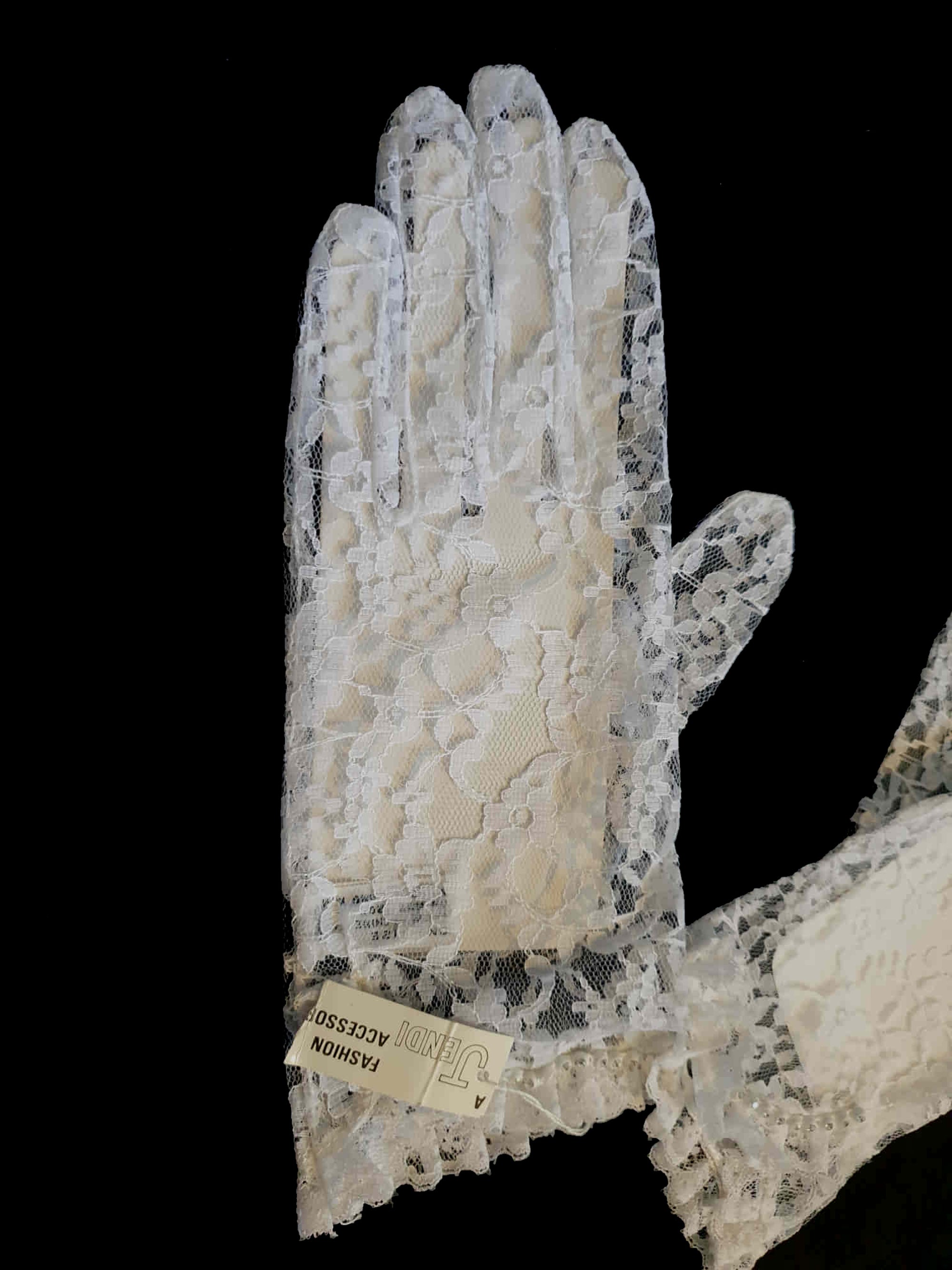 New old stock - beautiful lace bridal gloves with diamante trim, unsold stock from a former 1980s bridal boutique. White lace gloves are below-wrist length and have a shaped opening trimmed with more lace and a line of diamantes. 100% nylon. Made in Hong Kong for Jendi - 1980s.
