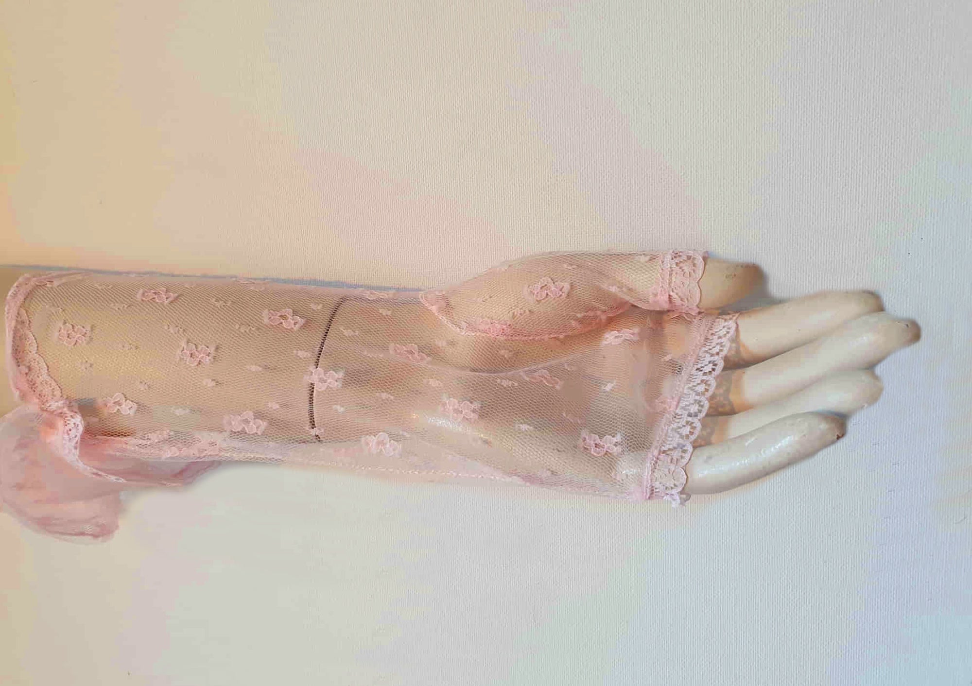 New old stock - Dainty lace mitts for a special occasion. Pale pink lace mitts or fingerless gloves are mid-forearm length. Trimmed with narrow lace at the edges. 100% nylon. Made in Hong Kong. No brand label. From a former 1980s bridal boutique. Mint condition - brand new and never used.
