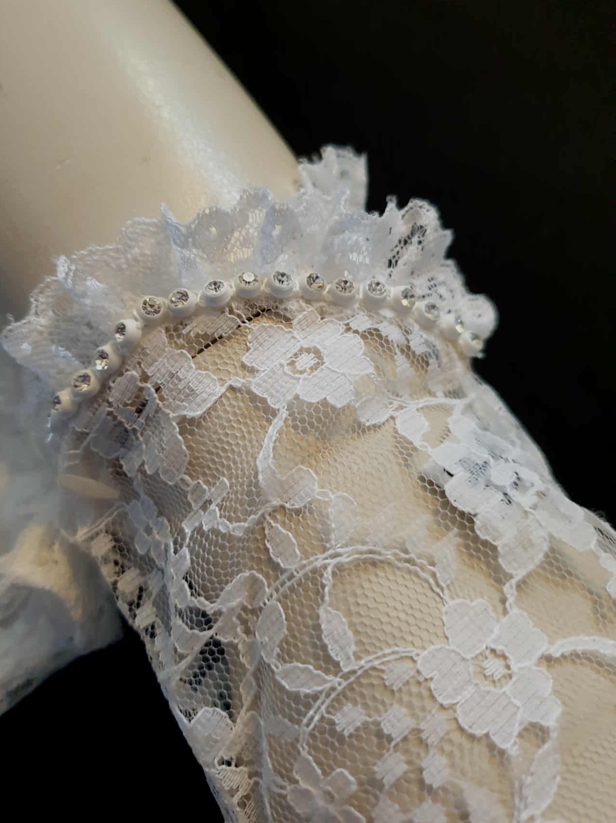 New old stock - beautiful lace bridal gloves with diamante trim, unsold stock from a former 1980s bridal boutique. White lace gloves are below-wrist length and have a shaped opening trimmed with more lace and a line of diamantes. 100% nylon. Made in Hong Kong for Jendi - 1980s.