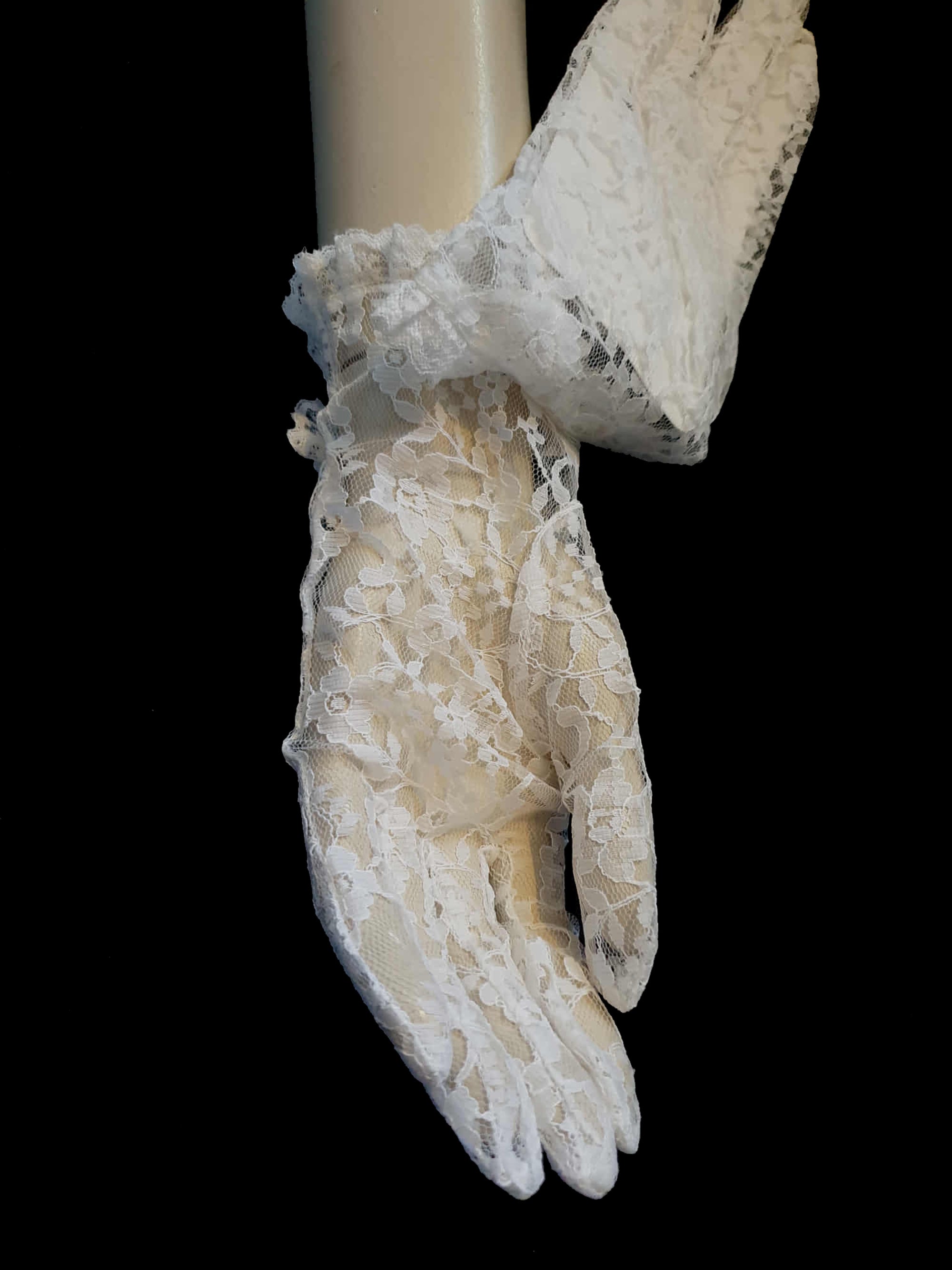New old stock - beautiful lace bridal gloves with diamante trim, unsold stock from a former 1980s bridal boutique. White lace gloves are below-wrist length and have a shaped opening trimmed with more lace and a line of diamantes. 100% nylon. Made in Hong Kong for Jendi - 1980s.