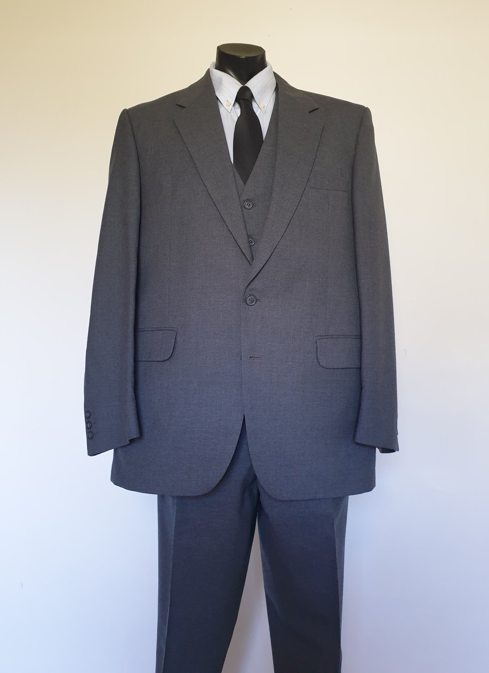 The suit jacket has notched lapels, flapped pockets, breast pocket, two button closure, three button sleeve trim and three interior pockets. It has two rear vents.
The vest has two pockets and five button closure. There is no belt for rear adjustment.
The trousers have straight legs, two front pleats at the waist, two diagonal side pockets, coin pocket and two buttoning rear pockets. 
The fabric is 80% wool, 20% polyester. Made by the iconic Fletcher Jones Australia. Conveniently dated 1-5-1990. Size 117R.