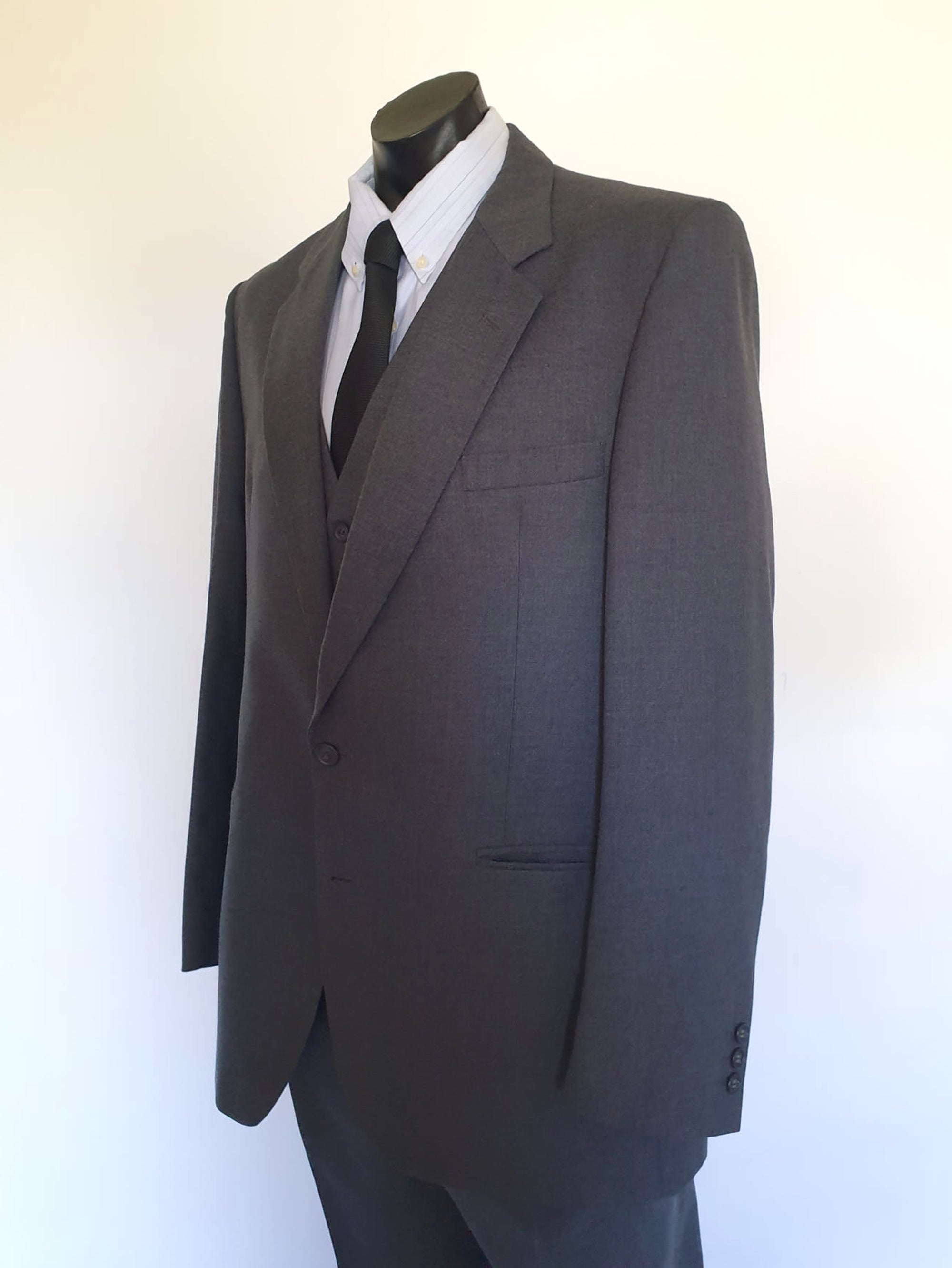 The suit jacket has notched lapels, flapped pockets, breast pocket, two button closure, three button sleeve trim and three interior pockets. It has two rear vents.
The vest has two pockets and five button closure. There is no belt for rear adjustment.
The trousers have straight legs, two front pleats at the waist, two diagonal side pockets, coin pocket and two buttoning rear pockets. 
The fabric is 80% wool, 20% polyester. Made by the iconic Fletcher Jones Australia. Conveniently dated 1-5-1990. Size 117R.