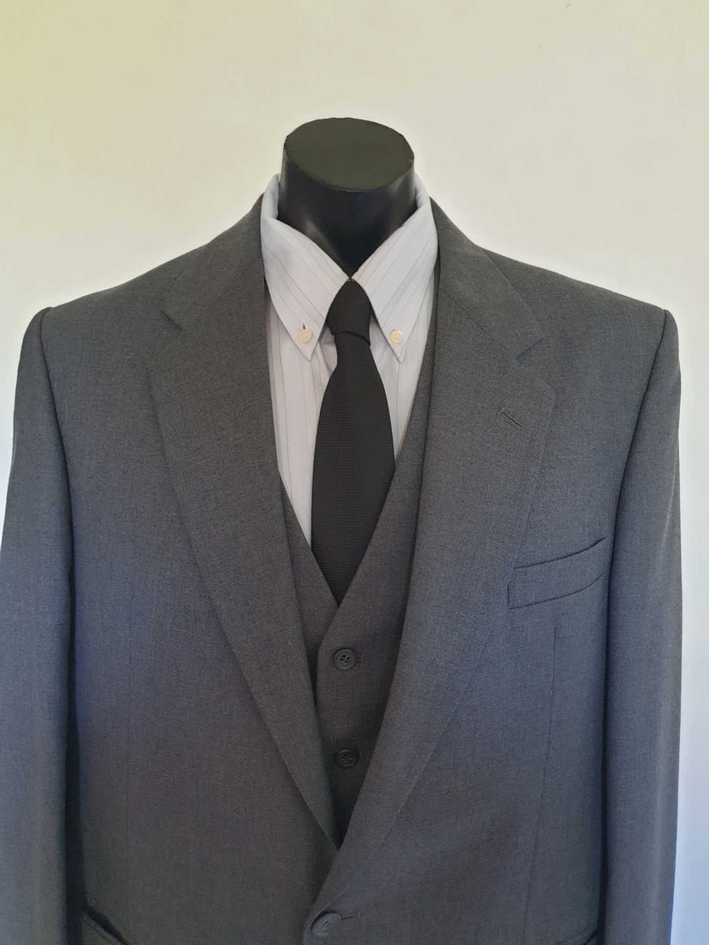 The suit jacket has notched lapels, flapped pockets, breast pocket, two button closure, three button sleeve trim and three interior pockets. It has two rear vents.
The vest has two pockets and five button closure. There is no belt for rear adjustment.
The trousers have straight legs, two front pleats at the waist, two diagonal side pockets, coin pocket and two buttoning rear pockets. 
The fabric is 80% wool, 20% polyester. Made by the iconic Fletcher Jones Australia. Conveniently dated 1-5-1990. Size 117R.