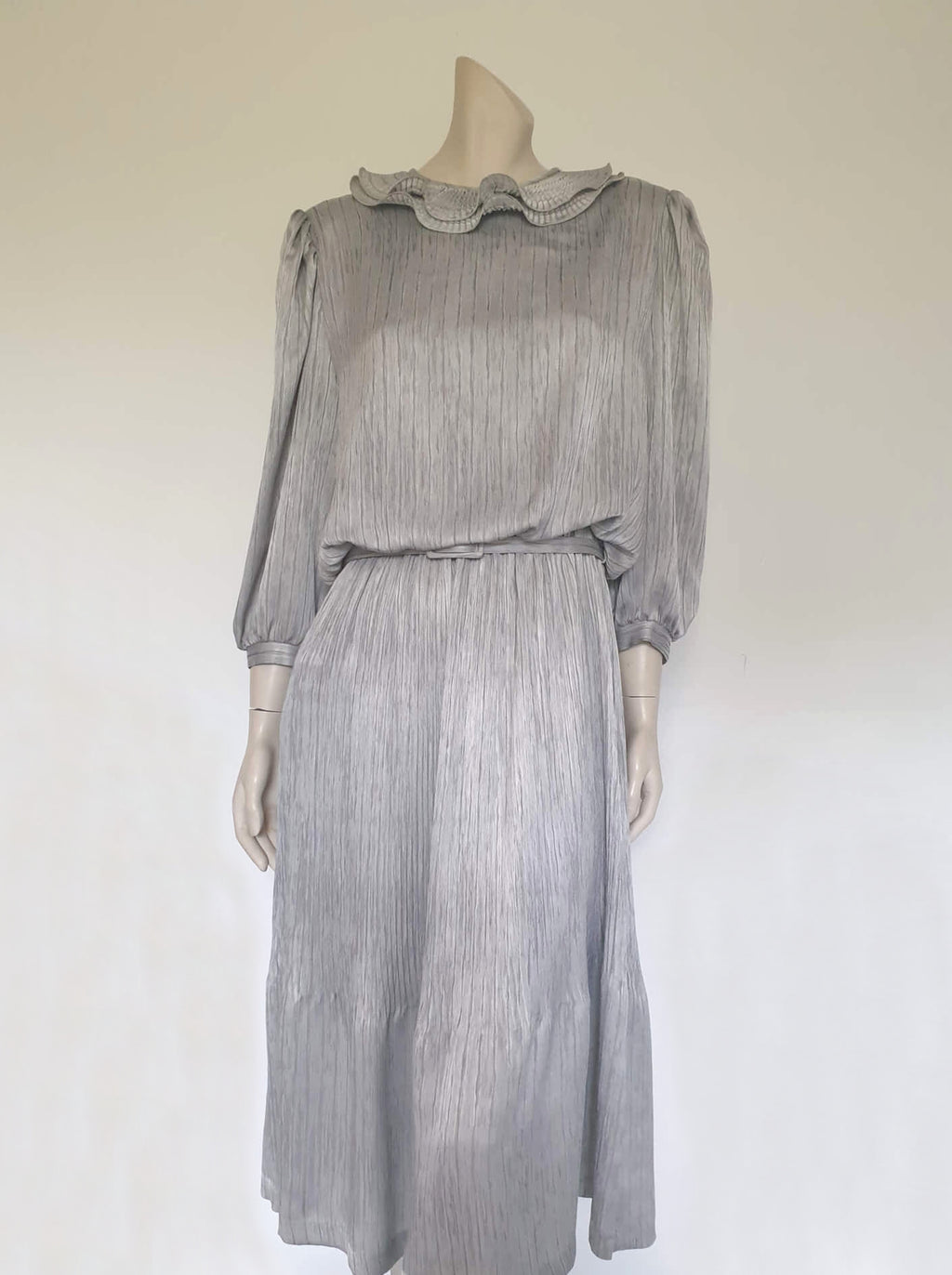 Beautiful and classy secretary style dress. Mid-calf length silver grey dress has three-quarter length buttoning sleeves and a circular ruffled collar. The skirt has very narrow permanent pleats to about knee level. The same pleated fabric has been used for the collar. The bodice is a full blouson look.  Brand is The Dress Company - 1980s. Medium