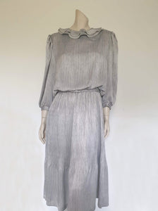 Beautiful and classy secretary style dress. Mid-calf length silver grey dress has three-quarter length buttoning sleeves and a circular ruffled collar. The skirt has very narrow permanent pleats to about knee level. The same pleated fabric has been used for the collar. The bodice is a full blouson look.  Brand is The Dress Company - 1980s. Medium