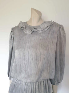 Beautiful and classy secretary style dress. Mid-calf length silver grey dress has three-quarter length buttoning sleeves and a circular ruffled collar. The skirt has very narrow permanent pleats to about knee level. The same pleated fabric has been used for the collar. The bodice is a full blouson look.  Brand is The Dress Company - 1980s. Medium