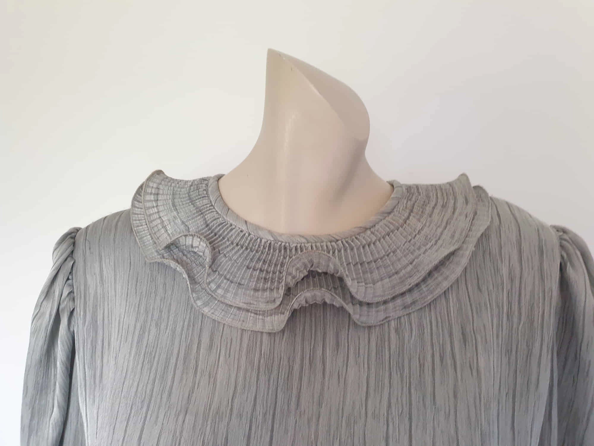 Beautiful and classy secretary style dress. Mid-calf length silver grey dress has three-quarter length buttoning sleeves and a circular ruffled collar. The skirt has very narrow permanent pleats to about knee level. The same pleated fabric has been used for the collar. The bodice is a full blouson look.  Brand is The Dress Company - 1980s. Medium