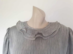 Beautiful and classy secretary style dress. Mid-calf length silver grey dress has three-quarter length buttoning sleeves and a circular ruffled collar. The skirt has very narrow permanent pleats to about knee level. The same pleated fabric has been used for the collar. The bodice is a full blouson look.  Brand is The Dress Company - 1980s. Medium