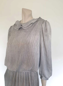Beautiful and classy secretary style dress. Mid-calf length silver grey dress has three-quarter length buttoning sleeves and a circular ruffled collar. The skirt has very narrow permanent pleats to about knee level. The same pleated fabric has been used for the collar. The bodice is a full blouson look.  Brand is The Dress Company - 1980s. Medium