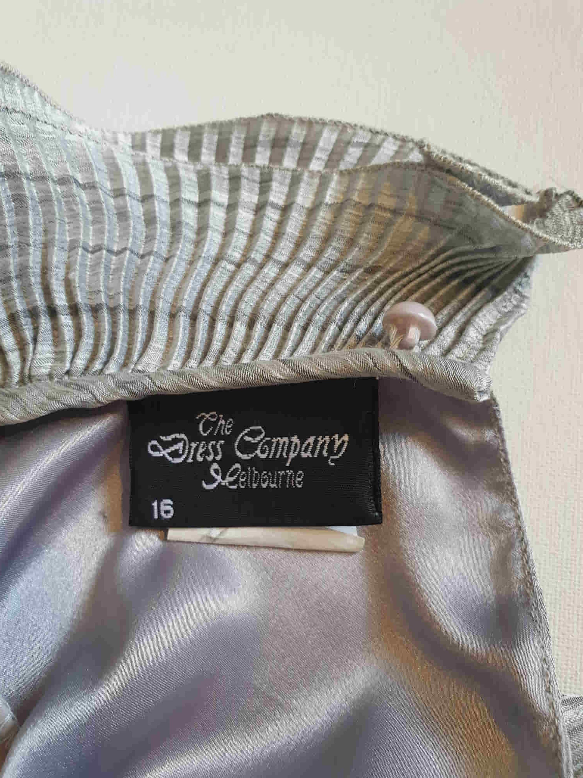 Beautiful and classy secretary style dress. Mid-calf length silver grey dress has three-quarter length buttoning sleeves and a circular ruffled collar. The skirt has very narrow permanent pleats to about knee level. The same pleated fabric has been used for the collar. The bodice is a full blouson look.  Brand is The Dress Company - 1980s. Medium