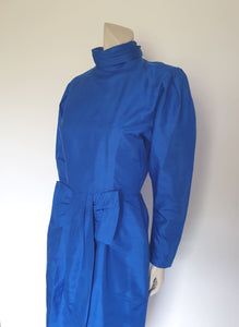 Screaming '80s winter formal dress from Argentinian born Sydney based designer Ewaldo Bock. Trimmed with an enormous bow at the front, this lower-calf  length dress features a high collar which closes at the back with three buttons and loops. The dress has long sleeves with dropped armholes pleated into the shoulder. The straight skirt has a shaped overlap at the front incorporated into the bow and a pleated rear vent. Closes with a zip at the back. The fabric is shantung silk.