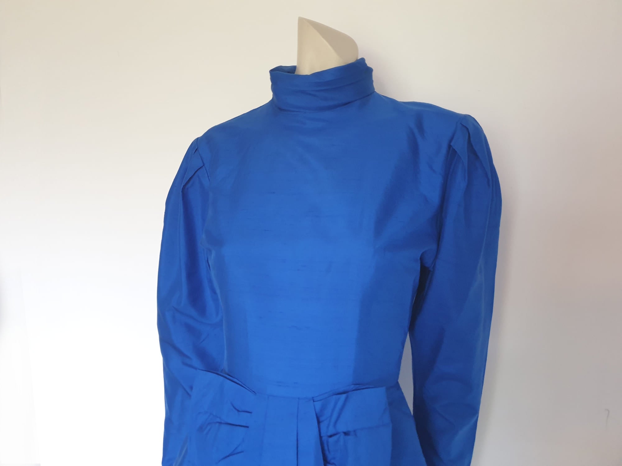 Screaming '80s winter formal dress from Argentinian born Sydney based designer Ewaldo Bock. Trimmed with an enormous bow at the front, this lower-calf  length dress features a high collar which closes at the back with three buttons and loops. The dress has long sleeves with dropped armholes pleated into the shoulder. The straight skirt has a shaped overlap at the front incorporated into the bow and a pleated rear vent. Closes with a zip at the back. The fabric is shantung silk.