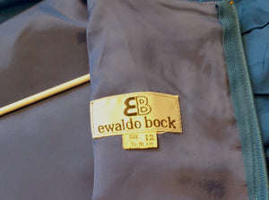 Screaming '80s winter formal dress from Argentinian born Sydney based designer Ewaldo Bock. Trimmed with an enormous bow at the front, this lower-calf  length dress features a high collar which closes at the back with three buttons and loops. The dress has long sleeves with dropped armholes pleated into the shoulder. The straight skirt has a shaped overlap at the front incorporated into the bow and a pleated rear vent. Closes with a zip at the back. The fabric is shantung silk.