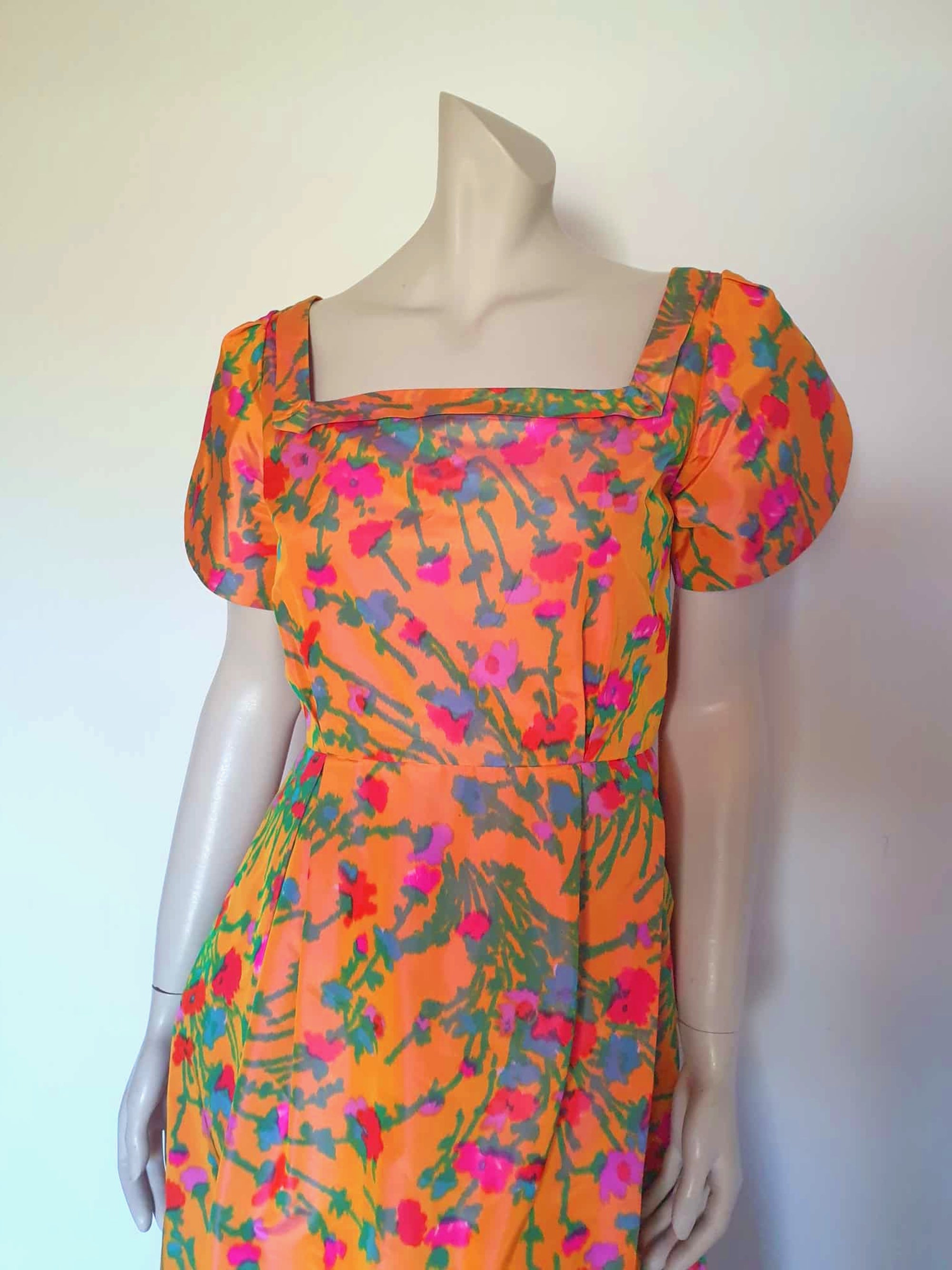 Superbly made gown in bright orange and pink florals in a very swishy parachute type fabric. 1950s style dress has wrap over sleeves exposing the vivid orange red lining. Square neckline. The skirt is wrapped at the front and pleated into the waist. It's very full at the back. Closes at the back with a nylon zip. The fabric is shot so that it can appear pink from different angles. The gown looks to have been made by a professional dressmaker  probably late 20th century. Medium