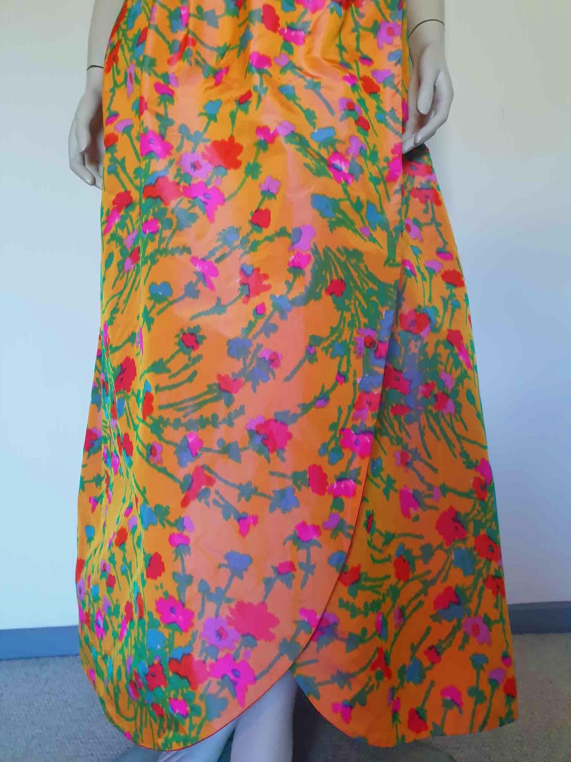 Superbly made gown in bright orange and pink florals in a very swishy parachute type fabric. 1950s style dress has wrap over sleeves exposing the vivid orange red lining. Square neckline. The skirt is wrapped at the front and pleated into the waist. It's very full at the back. Closes at the back with a nylon zip. The fabric is shot so that it can appear pink from different angles. The gown looks to have been made by a professional dressmaker  probably late 20th century. Medium