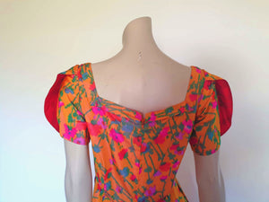 Superbly made gown in bright orange and pink florals in a very swishy parachute type fabric. 1950s style dress has wrap over sleeves exposing the vivid orange red lining. Square neckline. The skirt is wrapped at the front and pleated into the waist. It's very full at the back. Closes at the back with a nylon zip. The fabric is shot so that it can appear pink from different angles. The gown looks to have been made by a professional dressmaker  probably late 20th century. Medium