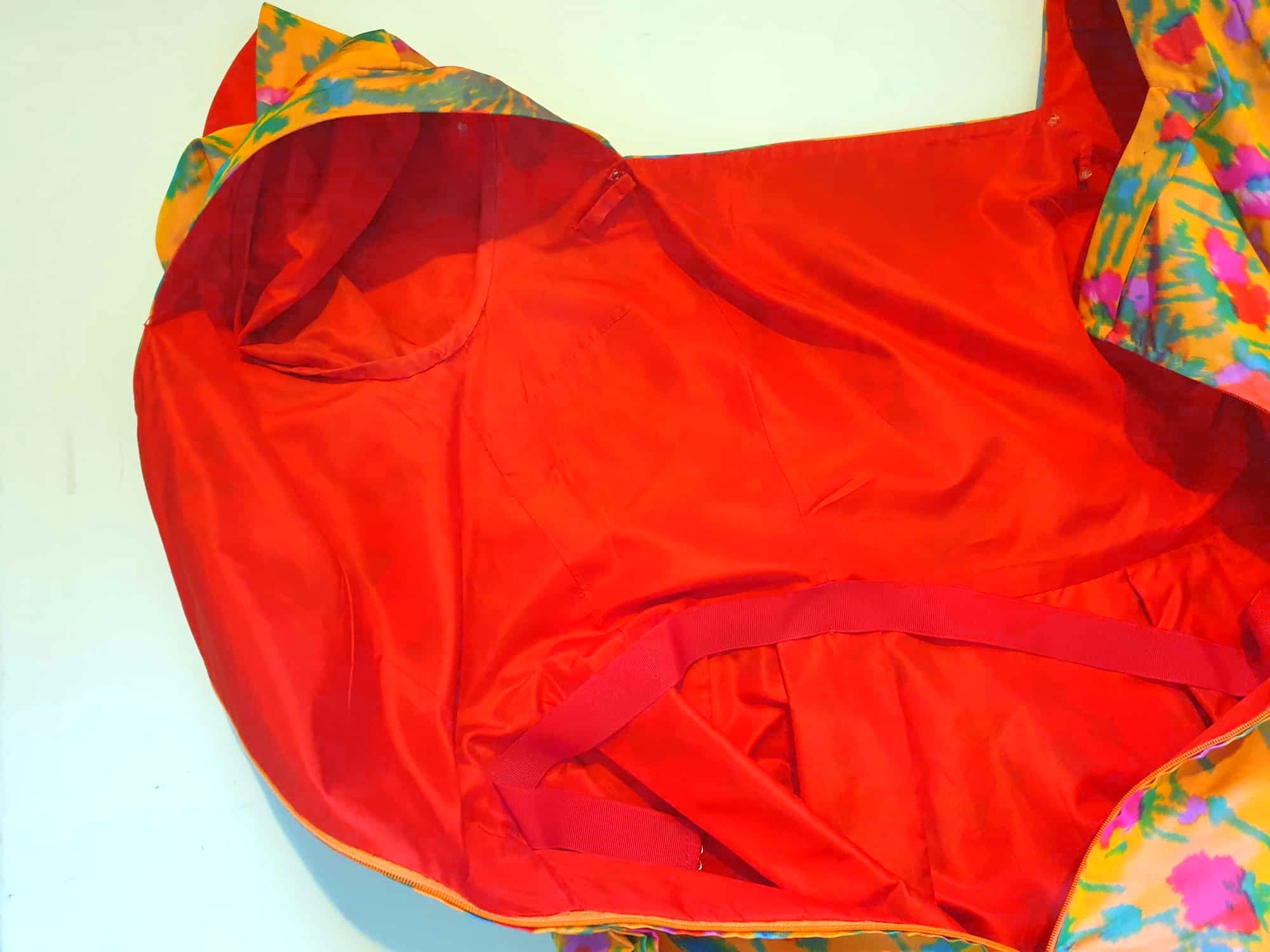 Superbly made gown in bright orange and pink florals in a very swishy parachute type fabric. 1950s style dress has wrap over sleeves exposing the vivid orange red lining. Square neckline. The skirt is wrapped at the front and pleated into the waist. It's very full at the back. Closes at the back with a nylon zip. The fabric is shot so that it can appear pink from different angles. The gown looks to have been made by a professional dressmaker  probably late 20th century. Medium