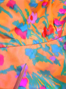 Superbly made gown in bright orange and pink florals in a very swishy parachute type fabric. 1950s style dress has wrap over sleeves exposing the vivid orange red lining. Square neckline. The skirt is wrapped at the front and pleated into the waist. It's very full at the back. Closes at the back with a nylon zip. The fabric is shot so that it can appear pink from different angles. The gown looks to have been made by a professional dressmaker  probably late 20th century. Medium