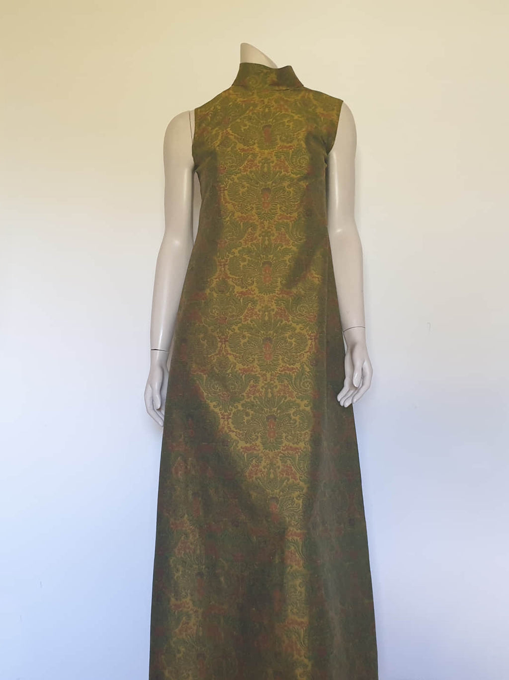 Gorgeous full length formal gown has a stylised Victorian style print in green and coral on a yellow-green ground and overall looks olive green. The fabric is stiff and has a sheen. It has a high standing collar. Closes at the back with a metal zip. The collar closes with hooks and eyes.  Fully lined. Custom made in Hong Kong by Jacky Taylor & Co. Late 1960s - early 1970s. Small.