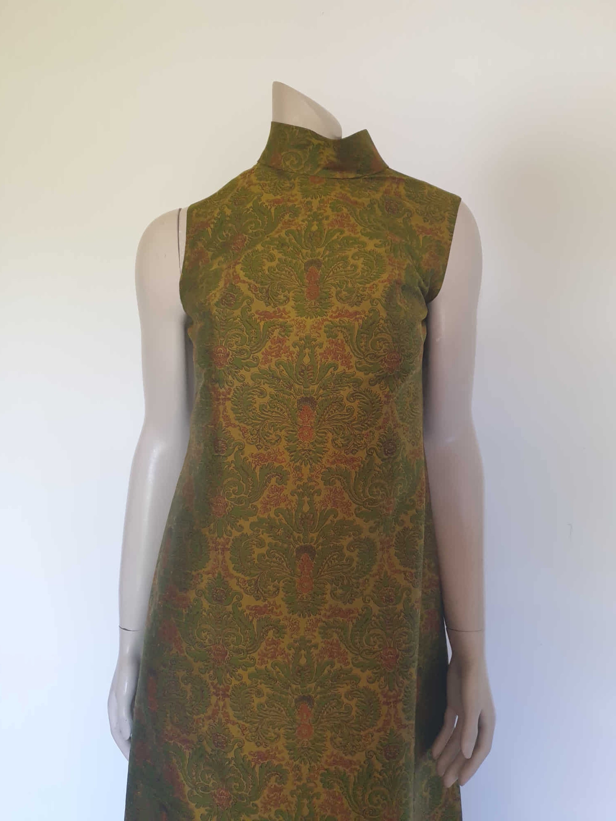Gorgeous full length formal gown has a stylised Victorian style print in green and coral on a yellow-green ground and overall looks olive green. The fabric is stiff and has a sheen. It has a high standing collar. Closes at the back with a metal zip. The collar closes with hooks and eyes.  Fully lined. Custom made in Hong Kong by Jacky Taylor & Co. Late 1960s - early 1970s. Small.