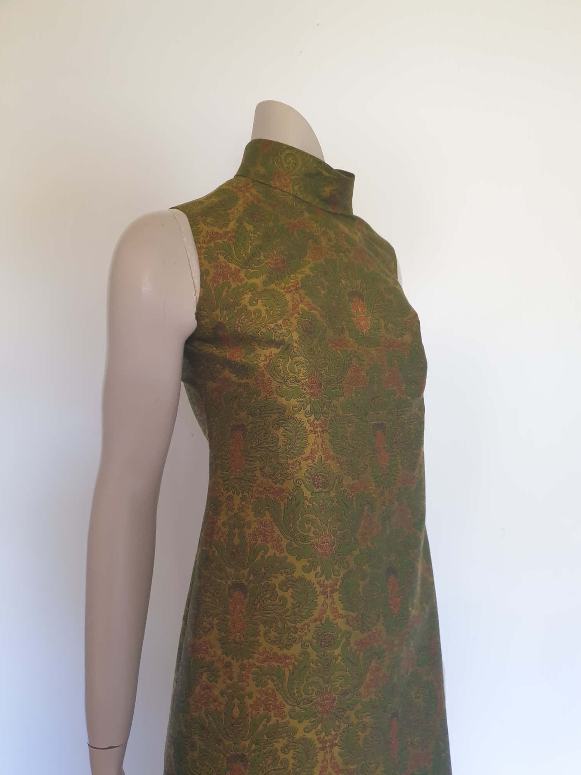 Gorgeous full length formal gown has a stylised Victorian style print in green and coral on a yellow-green ground and overall looks olive green. The fabric is stiff and has a sheen. It has a high standing collar. Closes at the back with a metal zip. The collar closes with hooks and eyes.  Fully lined. Custom made in Hong Kong by Jacky Taylor & Co. Late 1960s - early 1970s. Small.