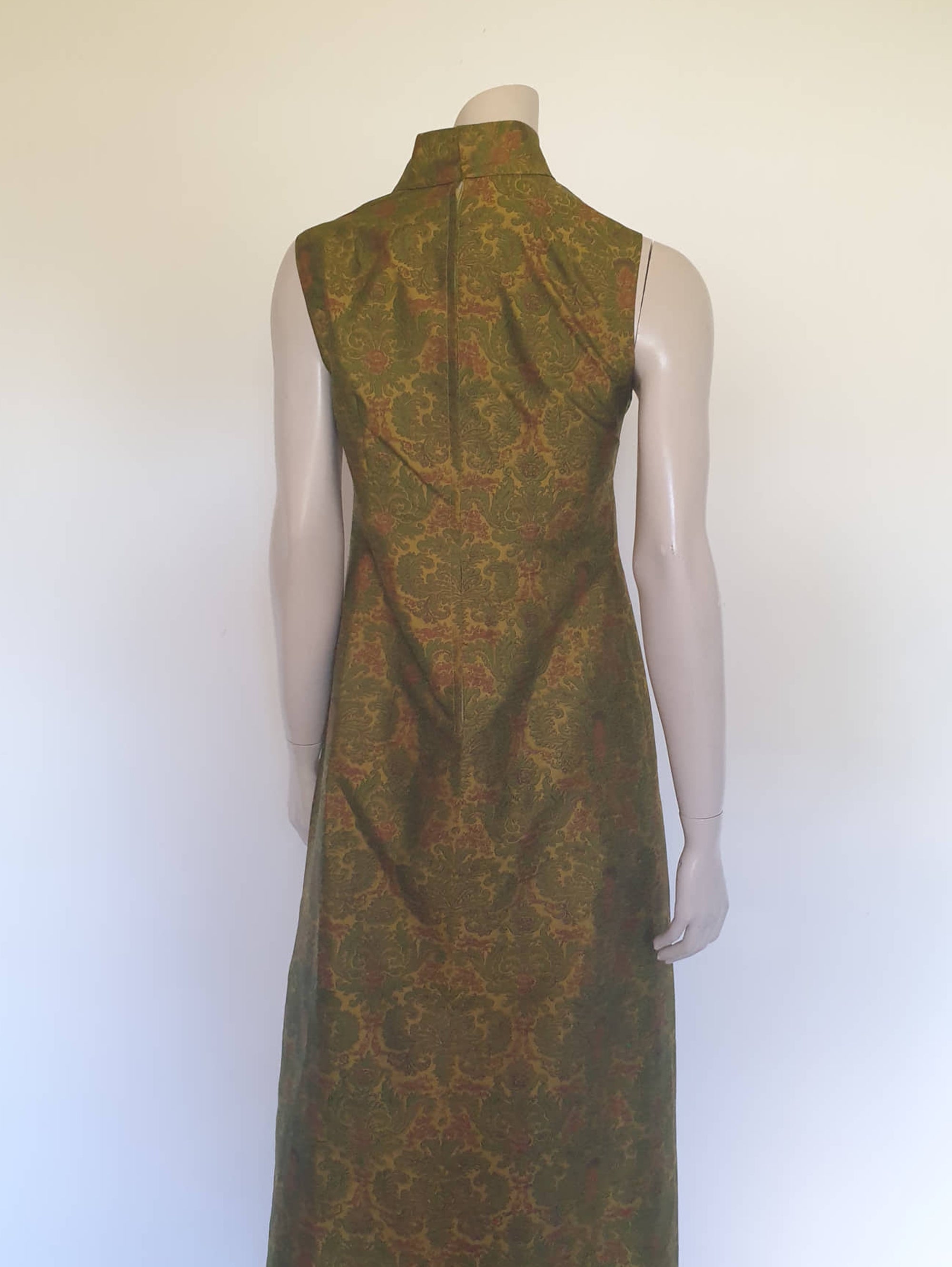Gorgeous full length formal gown has a stylised Victorian style print in green and coral on a yellow-green ground and overall looks olive green. The fabric is stiff and has a sheen. It has a high standing collar. Closes at the back with a metal zip. The collar closes with hooks and eyes.  Fully lined. Custom made in Hong Kong by Jacky Taylor & Co. Late 1960s - early 1970s. Small.