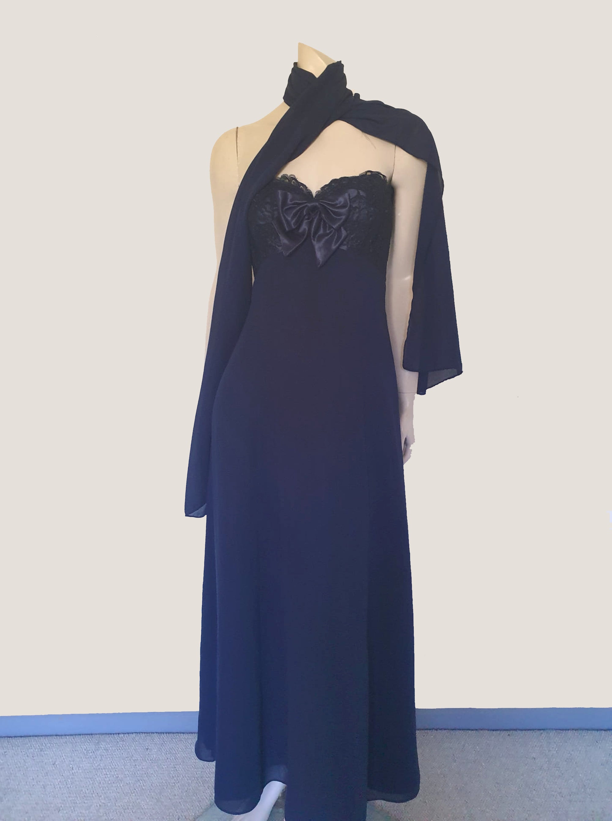Classy strapless formal dress with optional chiffon scarf. Navy blue strapless gown has a lace bodice with boning and is trimmed with a large satin bow at the bust. The long flared skirt is chiffon over a silky lining. Closes with a zip in the back. Fabric is 100% polyester. Made in Australia for Aurelie - 1980s. Extra Small.