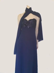 Classy strapless formal dress with optional chiffon scarf. Navy blue strapless gown has a lace bodice with boning and is trimmed with a large satin bow at the bust. The long flared skirt is chiffon over a silky lining. Closes with a zip in the back. Fabric is 100% polyester. Made in Australia for Aurelie - 1980s. Extra Small.