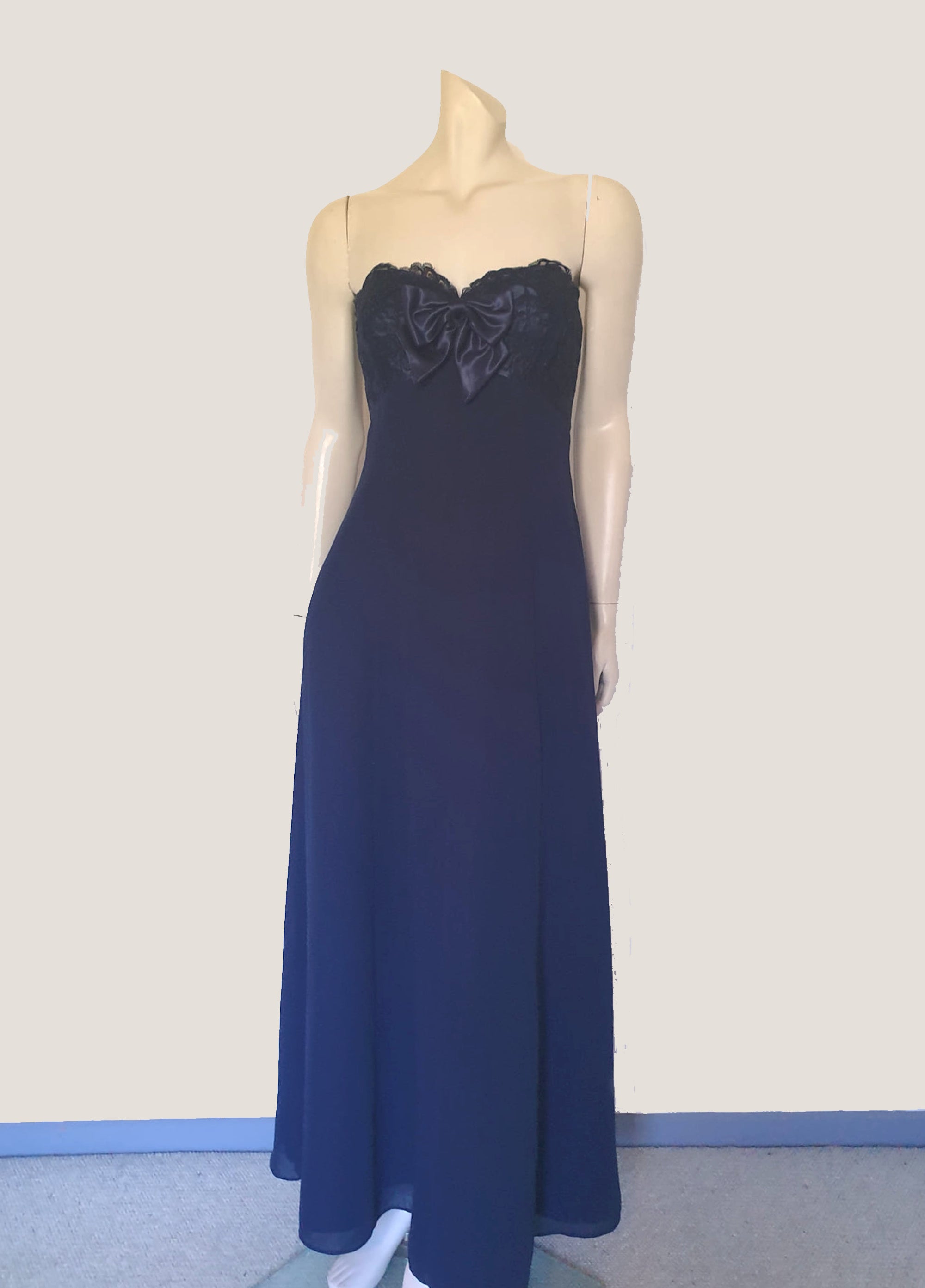 Classy strapless formal dress with optional chiffon scarf. Navy blue strapless gown has a lace bodice with boning and is trimmed with a large satin bow at the bust. The long flared skirt is chiffon over a silky lining. Closes with a zip in the back. Fabric is 100% polyester. Made in Australia for Aurelie - 1980s. Extra Small.