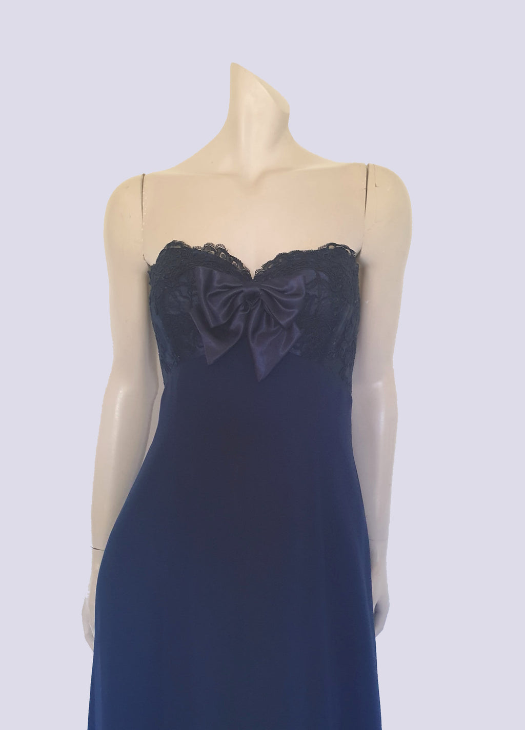 Classy strapless formal dress with optional chiffon scarf. Navy blue strapless gown has a lace bodice with boning and is trimmed with a large satin bow at the bust. The long flared skirt is chiffon over a silky lining. Closes with a zip in the back. Fabric is 100% polyester. Made in Australia for Aurelie - 1980s. Extra Small.