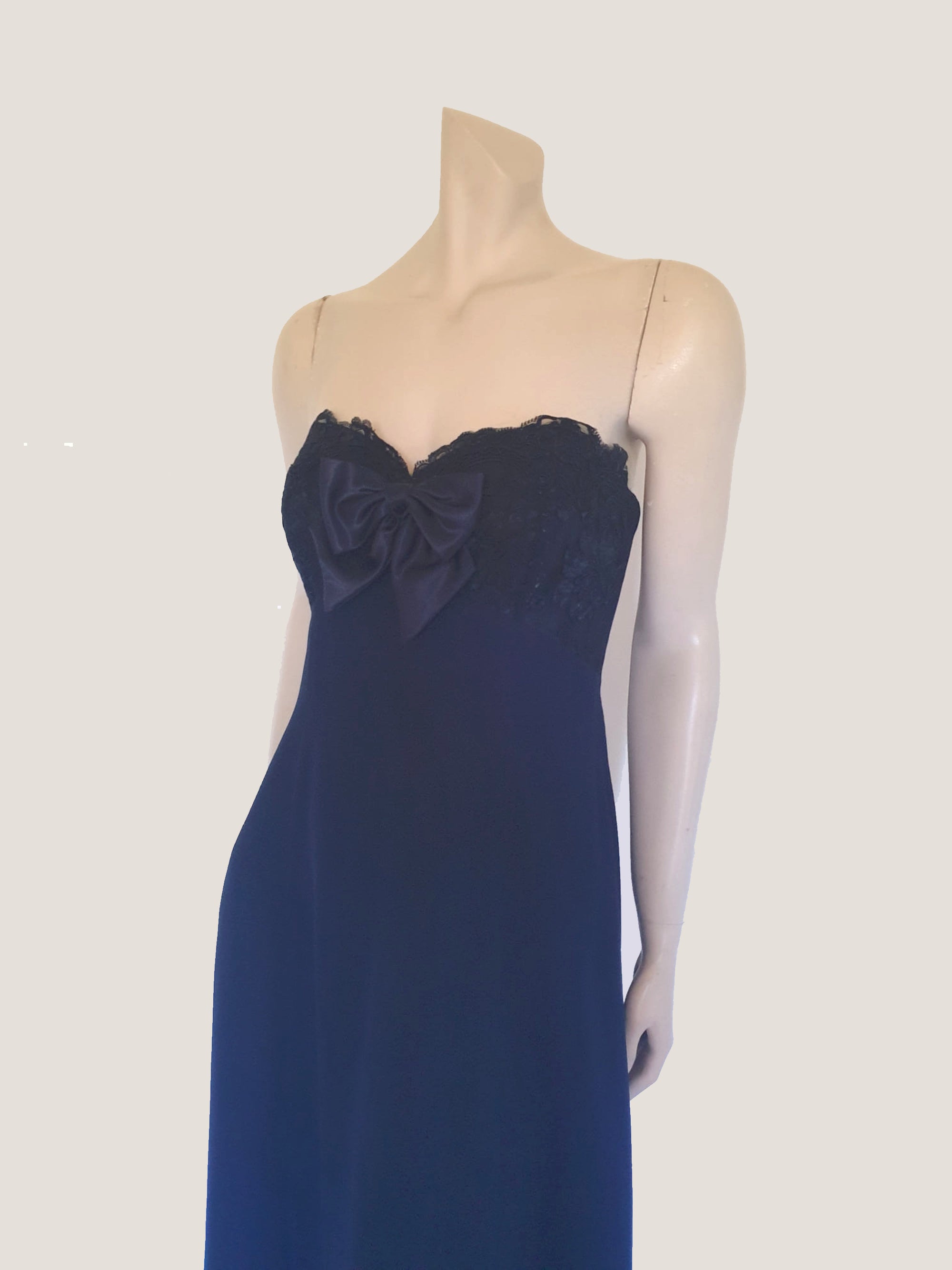 Classy strapless formal dress with optional chiffon scarf. Navy blue strapless gown has a lace bodice with boning and is trimmed with a large satin bow at the bust. The long flared skirt is chiffon over a silky lining. Closes with a zip in the back. Fabric is 100% polyester. Made in Australia for Aurelie - 1980s. Extra Small.
