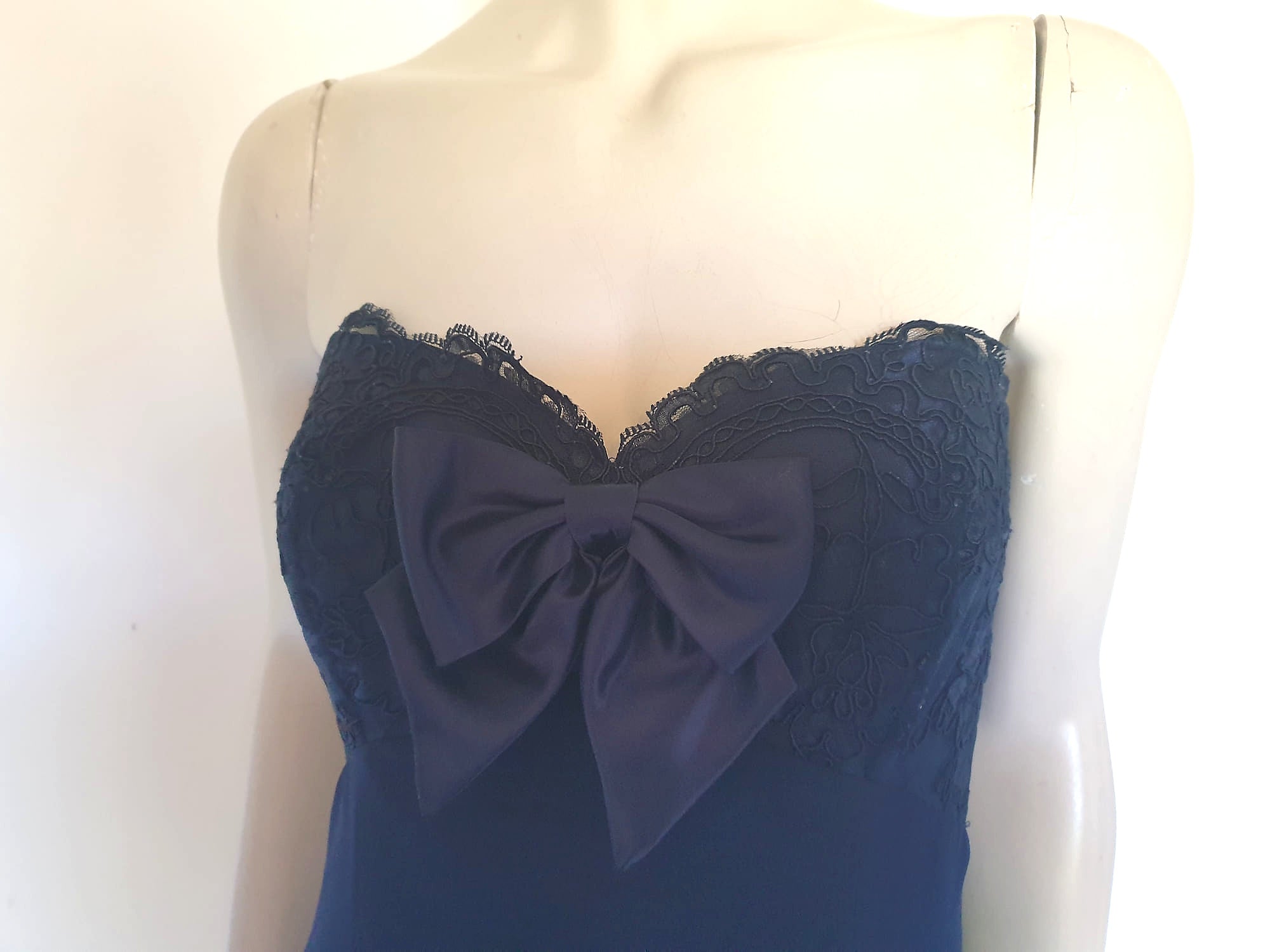 Classy strapless formal dress with optional chiffon scarf. Navy blue strapless gown has a lace bodice with boning and is trimmed with a large satin bow at the bust. The long flared skirt is chiffon over a silky lining. Closes with a zip in the back. Fabric is 100% polyester. Made in Australia for Aurelie - 1980s. Extra Small.