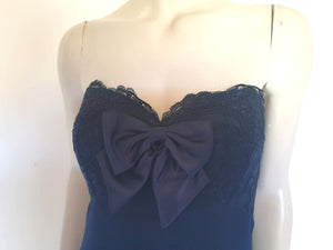 Classy strapless formal dress with optional chiffon scarf. Navy blue strapless gown has a lace bodice with boning and is trimmed with a large satin bow at the bust. The long flared skirt is chiffon over a silky lining. Closes with a zip in the back. Fabric is 100% polyester. Made in Australia for Aurelie - 1980s. Extra Small.