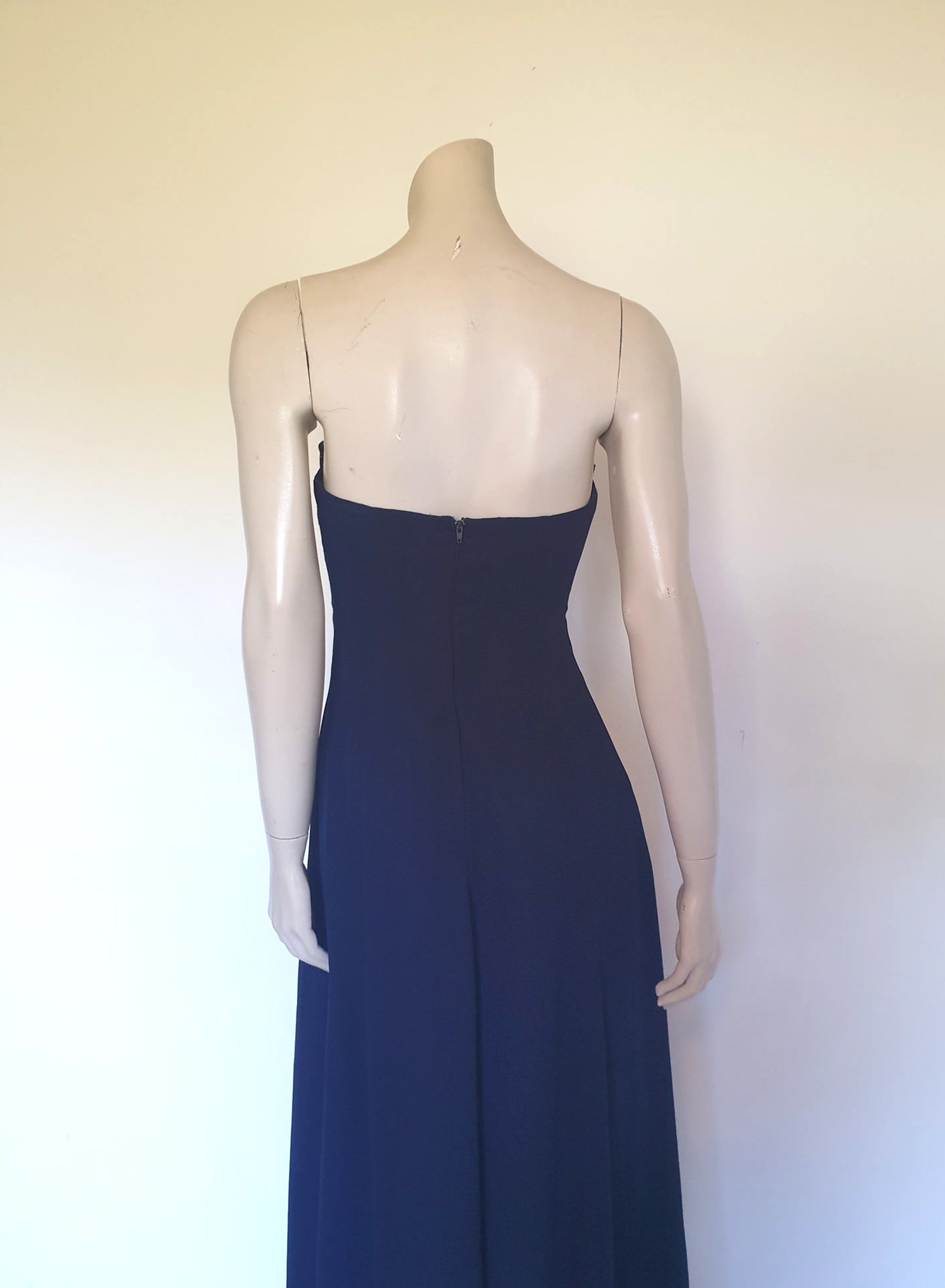 Classy strapless formal dress with optional chiffon scarf. Navy blue strapless gown has a lace bodice with boning and is trimmed with a large satin bow at the bust. The long flared skirt is chiffon over a silky lining. Closes with a zip in the back. Fabric is 100% polyester. Made in Australia for Aurelie - 1980s. Extra Small.