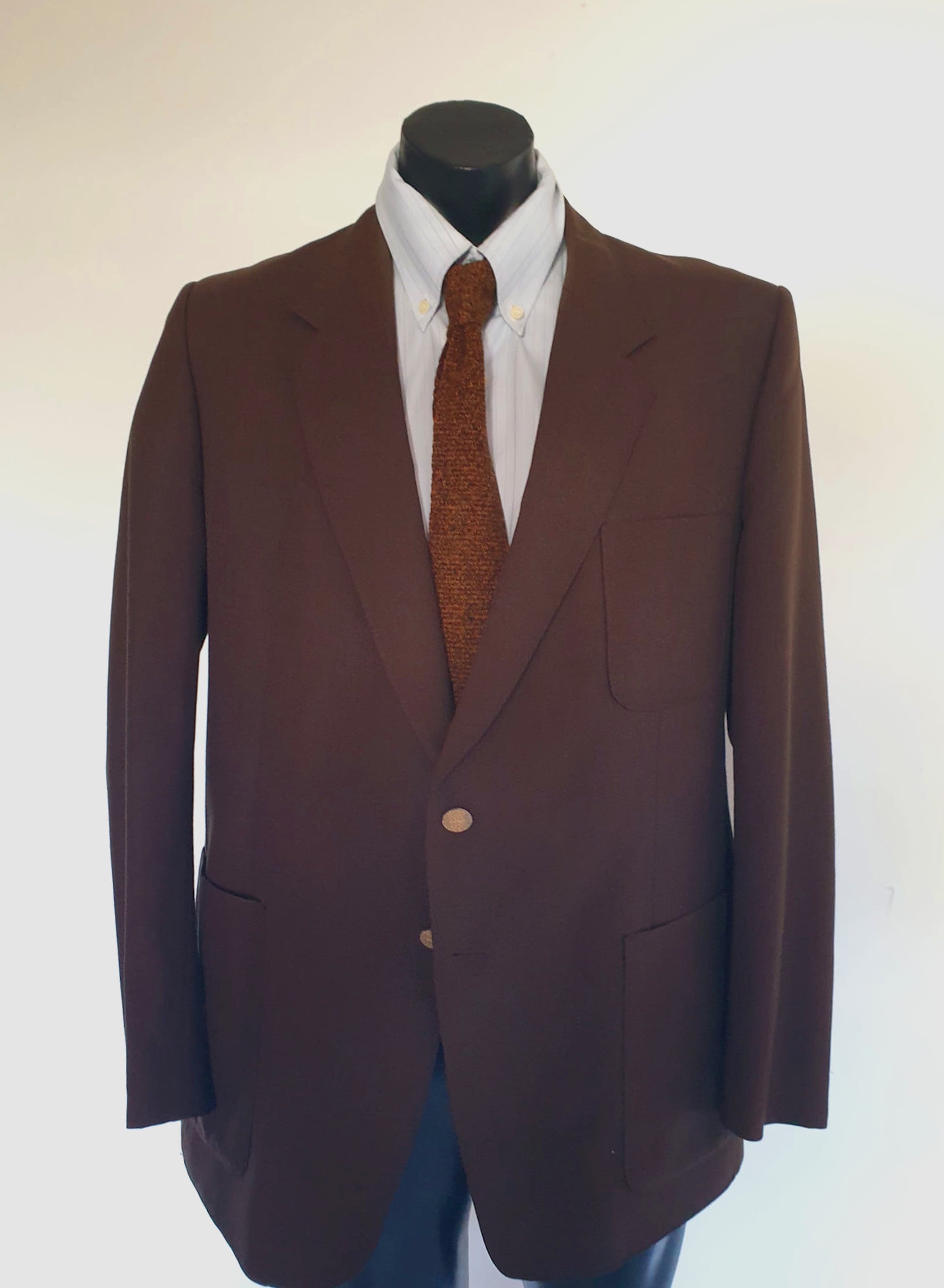 1970s blazer is chocolate brown and has notched lapels. It sports pewter coloured metal buttons featuring a heraldic crest. Three patch pockets at the front, one has a coin pocket. Three interior pockets. One button sleeve trim and two button closure. Rear vent. Fabric is 55% polyester, 45% wool. Lining appears to be rayon. Brand is the well known Australian tailoring company Stafford Ellinson - 1970s. 46RXL