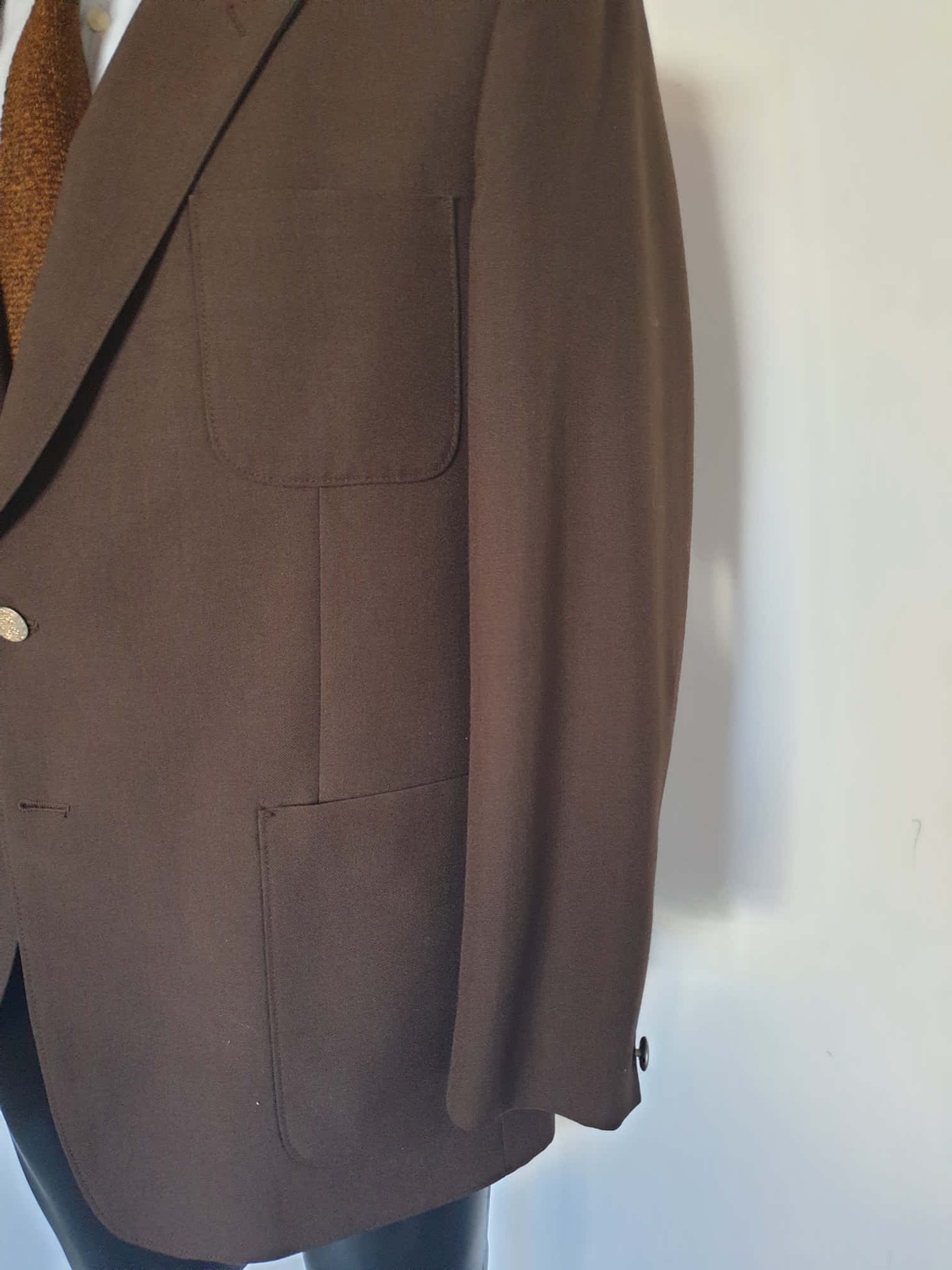 1970s blazer is chocolate brown and has notched lapels. It sports pewter coloured metal buttons featuring a heraldic crest. Three patch pockets at the front, one has a coin pocket. Three interior pockets. One button sleeve trim and two button closure. Rear vent. Fabric is 55% polyester, 45% wool. Lining appears to be rayon. Brand is the well known Australian tailoring company Stafford Ellinson - 1970s. 46RXL