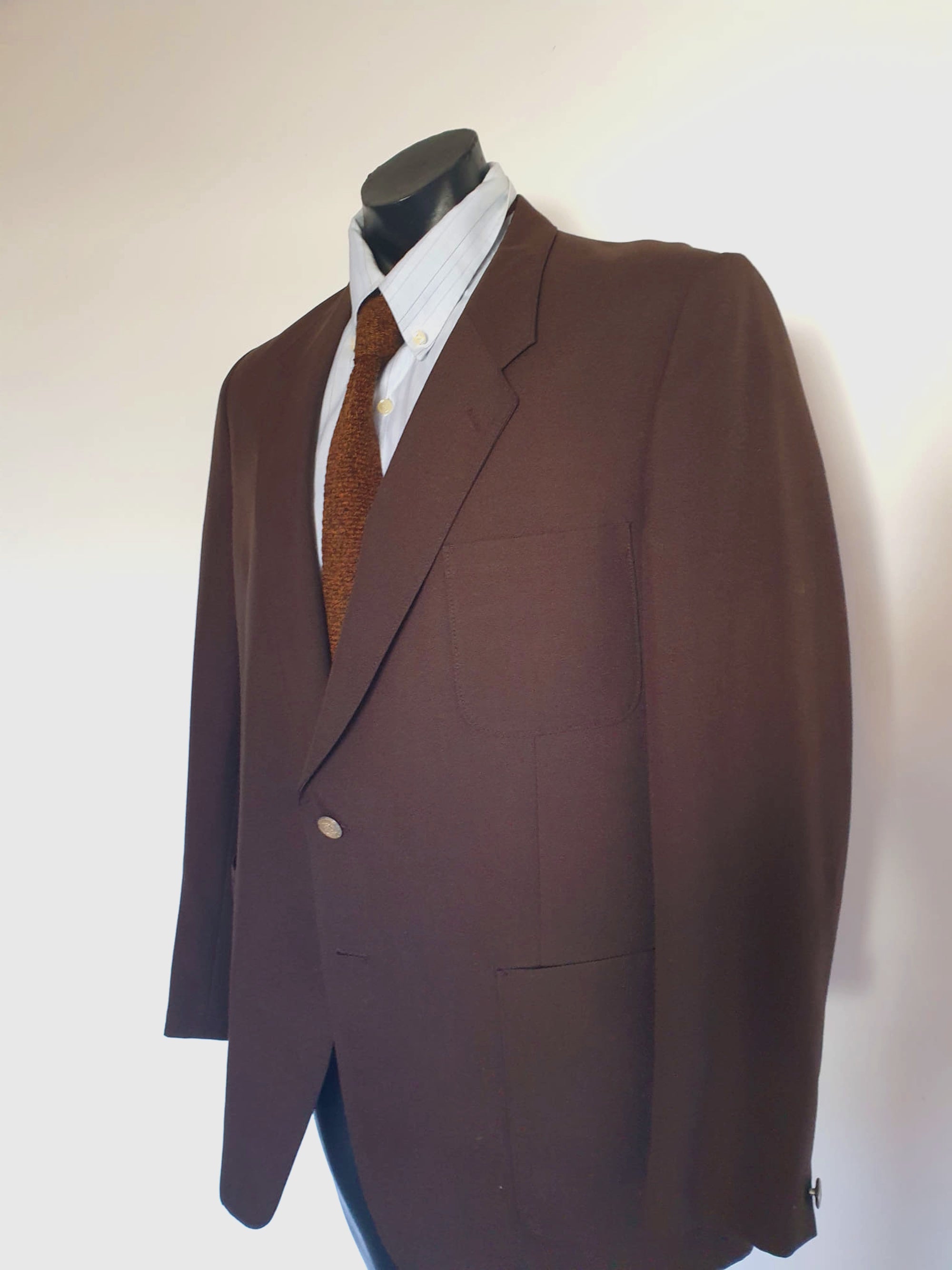1970s blazer is chocolate brown and has notched lapels. It sports pewter coloured metal buttons featuring a heraldic crest. Three patch pockets at the front, one has a coin pocket. Three interior pockets. One button sleeve trim and two button closure. Rear vent. Fabric is 55% polyester, 45% wool. Lining appears to be rayon. Brand is the well known Australian tailoring company Stafford Ellinson - 1970s. 46RXL