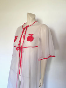 Super cute sheer white robe has red apples appliqued over the bust. The robe has full, elbow-length flutter sleeves and all edges are bound with red extending into ties at the neck and bust.   Ankle length. Fabric is polyamide (nylon). Made in Argentina. No brand label - 1970s. Medium