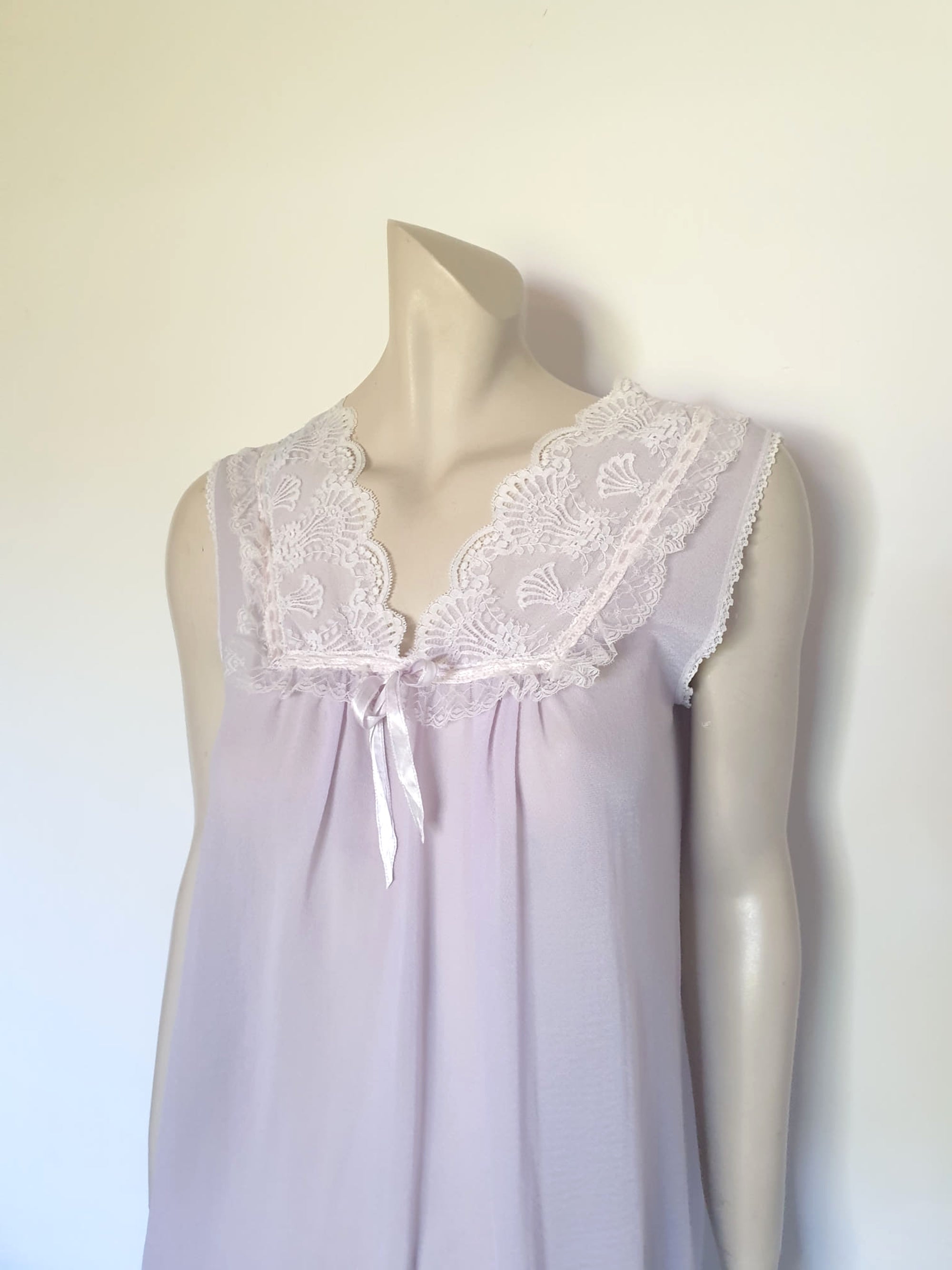 Pretty pale mauve crepe nightgown and robe set has a lace yoke tying at the neck with a ribbon on both the gown and robe. Pleas note: the colour is lighter than it appears in the photos. Above-knee length set has a high V neck and lace and pink ribbon trim at the yoke and sleeves. Hemline is also lace trimmed.  The robe has short sleeves, the gown is sleeveless. Fabric is nylon crepe. Brand is Irene - 1970s. Medium.