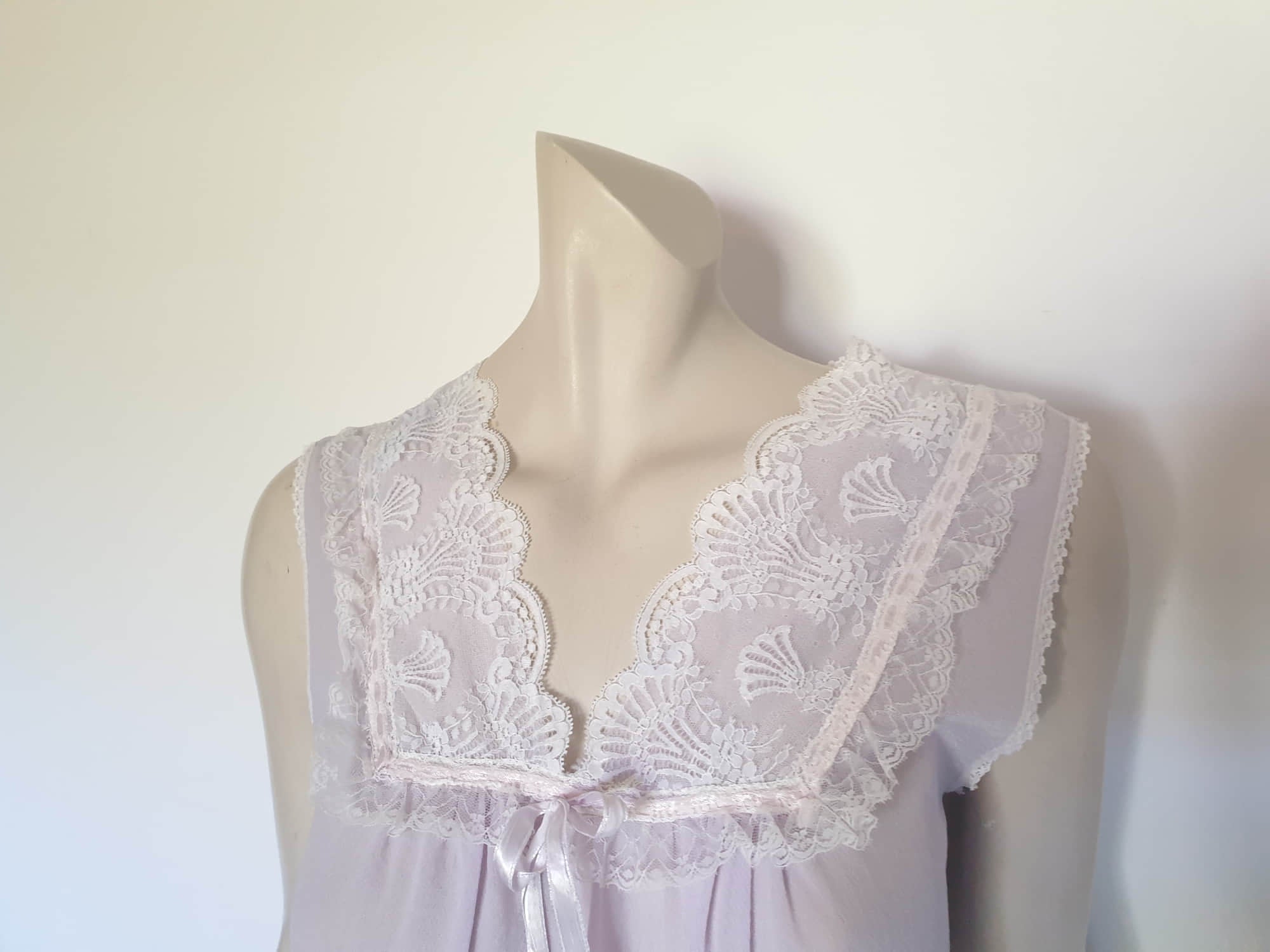 Pretty pale mauve crepe nightgown and robe set has a lace yoke tying at the neck with a ribbon on both the gown and robe. Pleas note: the colour is lighter than it appears in the photos. Above-knee length set has a high V neck and lace and pink ribbon trim at the yoke and sleeves. Hemline is also lace trimmed.  The robe has short sleeves, the gown is sleeveless. Fabric is nylon crepe. Brand is Irene - 1970s. Medium.