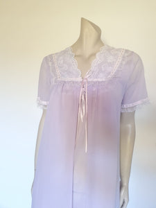 Pretty pale mauve crepe nightgown and robe set has a lace yoke tying at the neck with a ribbon on both the gown and robe. Pleas note: the colour is lighter than it appears in the photos. Above-knee length set has a high V neck and lace and pink ribbon trim at the yoke and sleeves. Hemline is also lace trimmed.  The robe has short sleeves, the gown is sleeveless. Fabric is nylon crepe. Brand is Irene - 1970s. Medium.