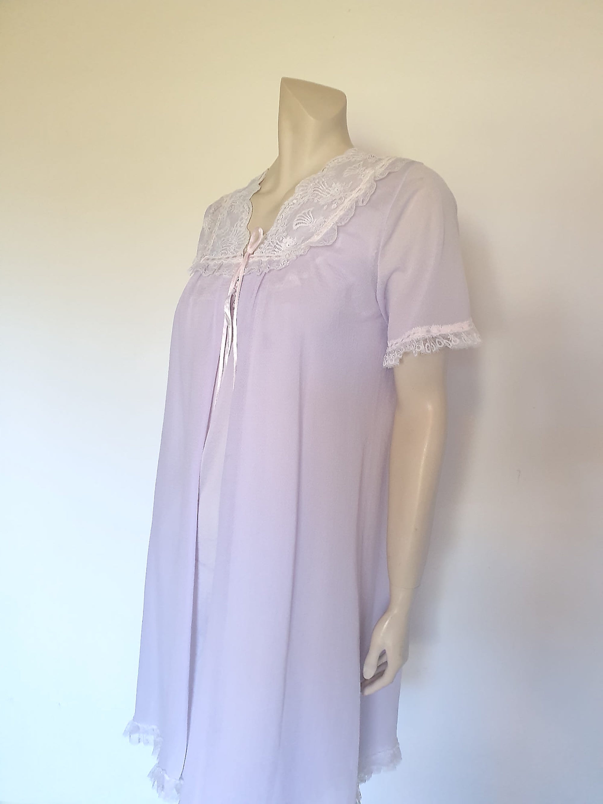 Pretty pale mauve crepe nightgown and robe set has a lace yoke tying at the neck with a ribbon on both the gown and robe. Pleas note: the colour is lighter than it appears in the photos. Above-knee length set has a high V neck and lace and pink ribbon trim at the yoke and sleeves. Hemline is also lace trimmed.  The robe has short sleeves, the gown is sleeveless. Fabric is nylon crepe. Brand is Irene - 1970s. Medium.