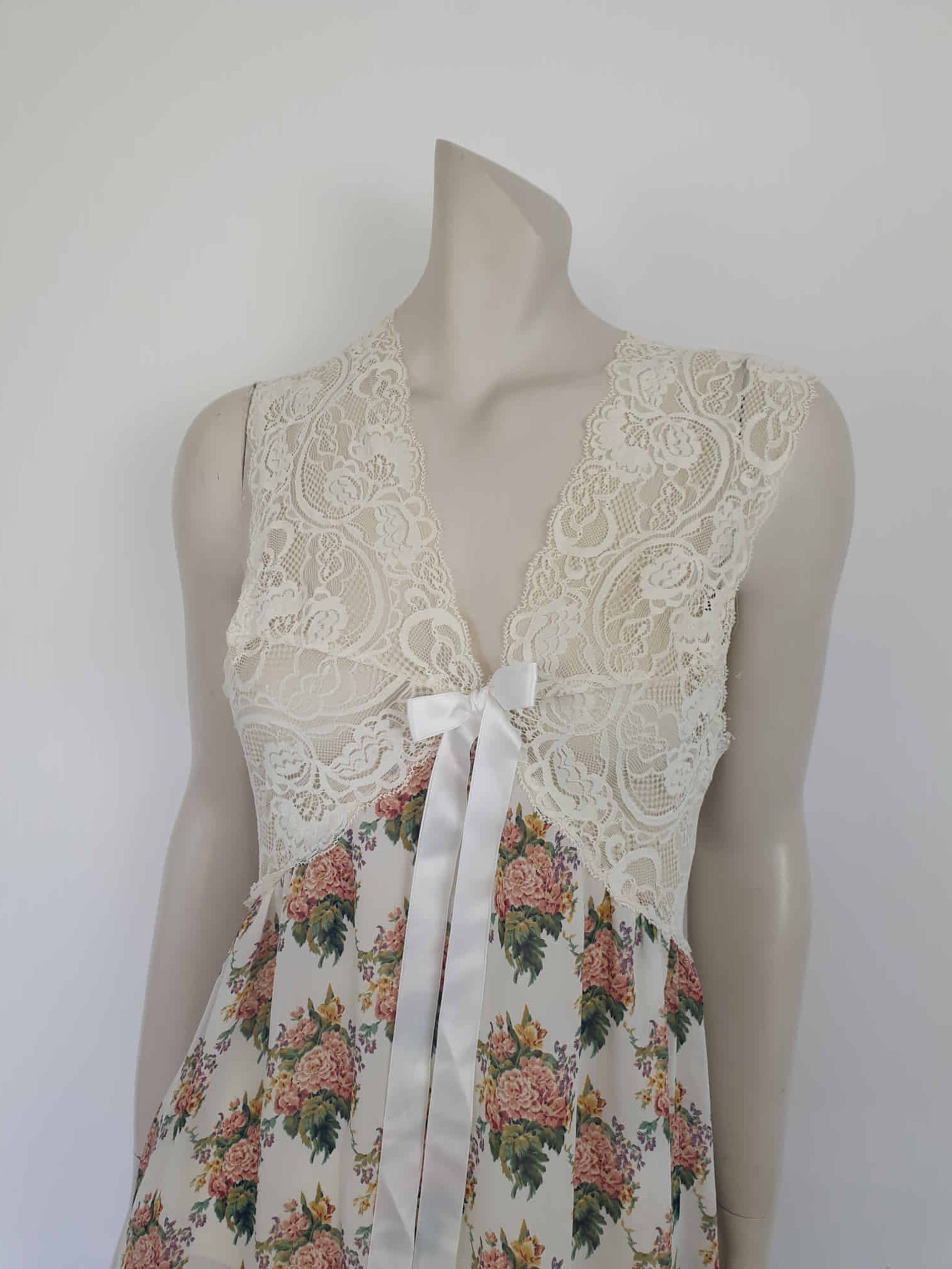 Beautiful and elegant nightgown. Long nightgown has a pink and green floral print on a cream ground. The fitted front bodice is cream stretch lace. There's also panel of lace at centre back. Trimmed with a satin bow and long ribbons beneath the bust. There are no labels, but the fabric is polyester georgette. 1980s. Bust 92 cm (36")